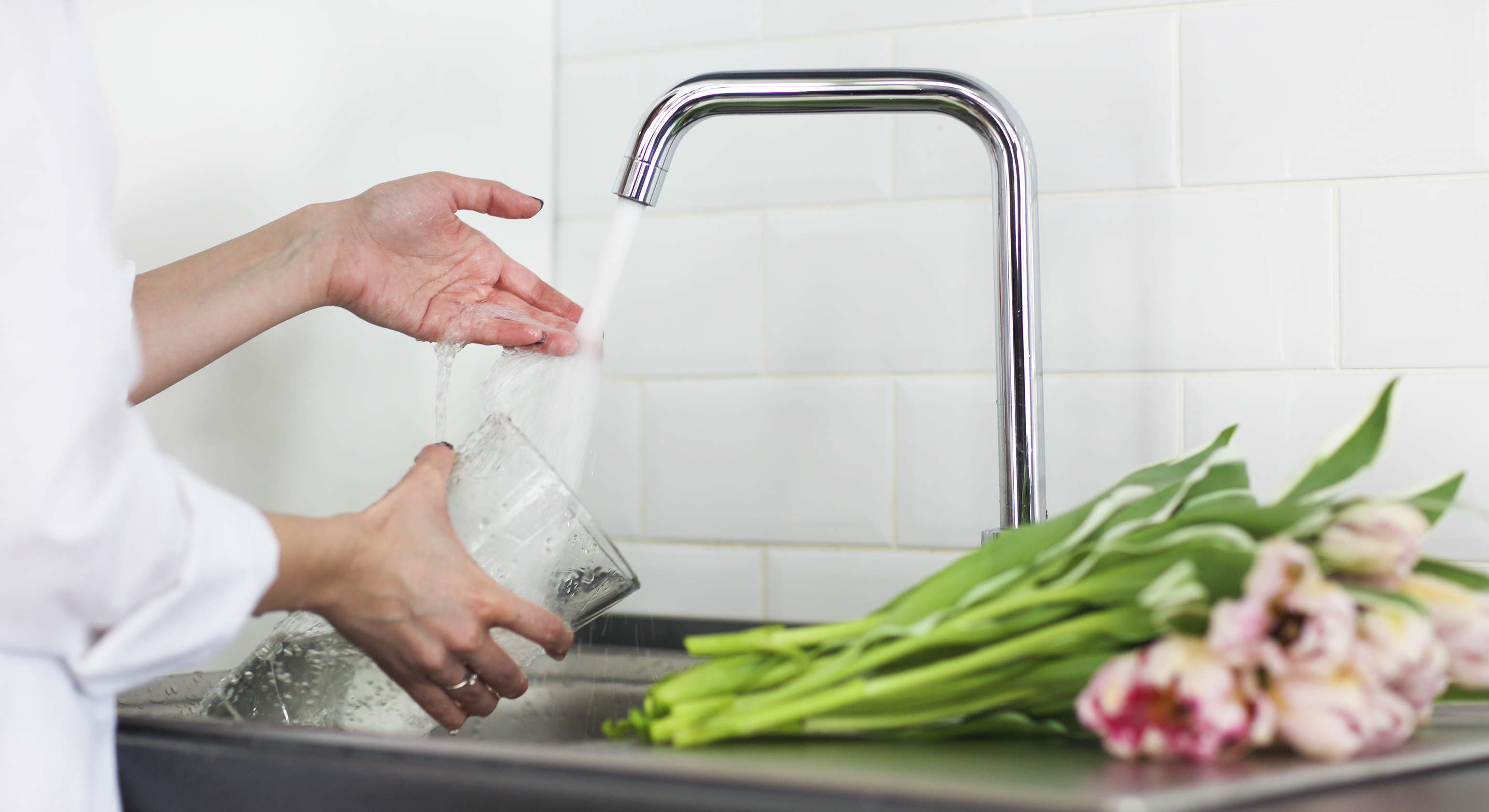 Femme versant de l'eau douce dans un vase en verre avec de la tulipe sur le côté