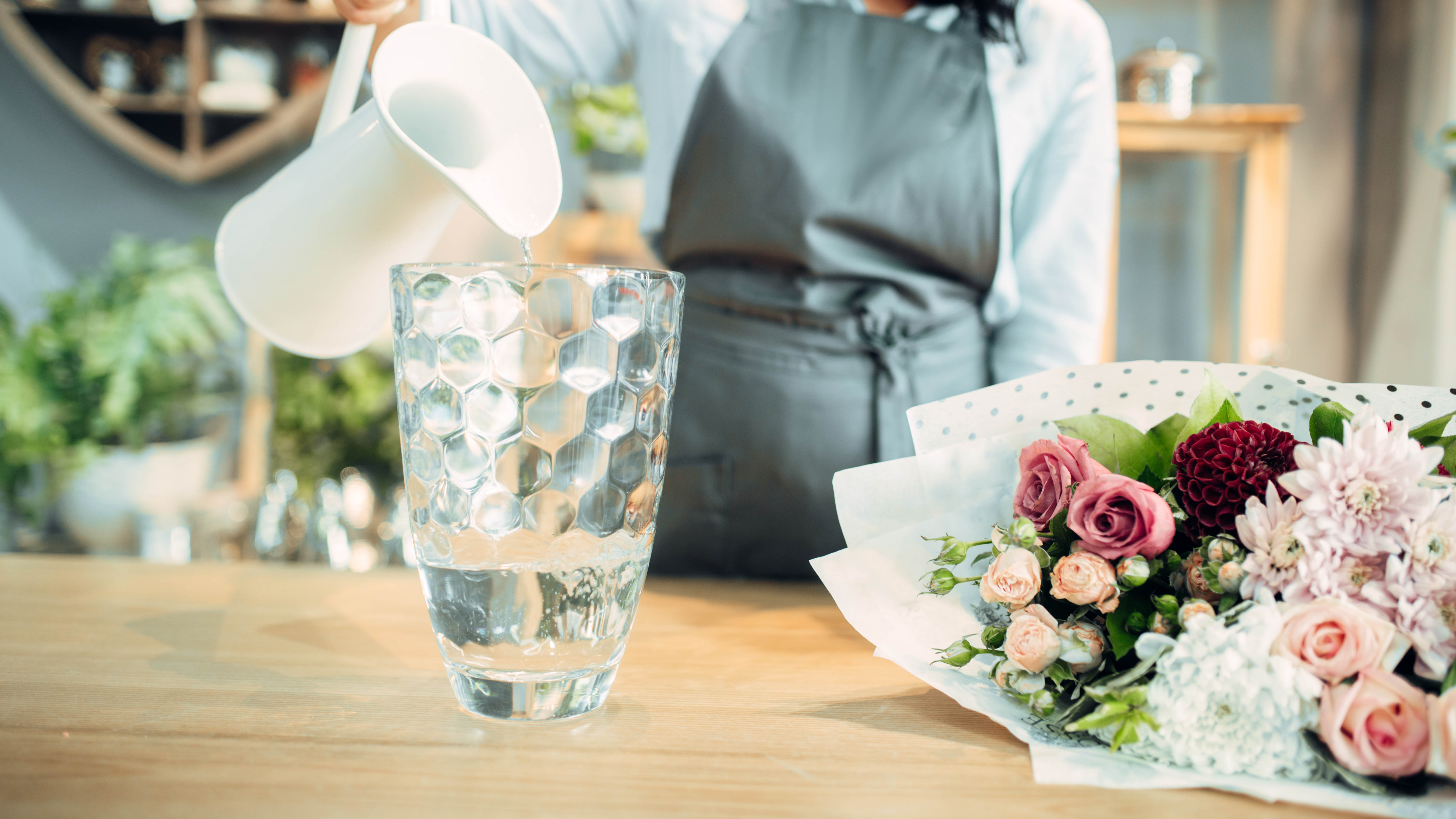 Un pichet versant de l'eau dans un vase à côté d'un bouquet de fleurs