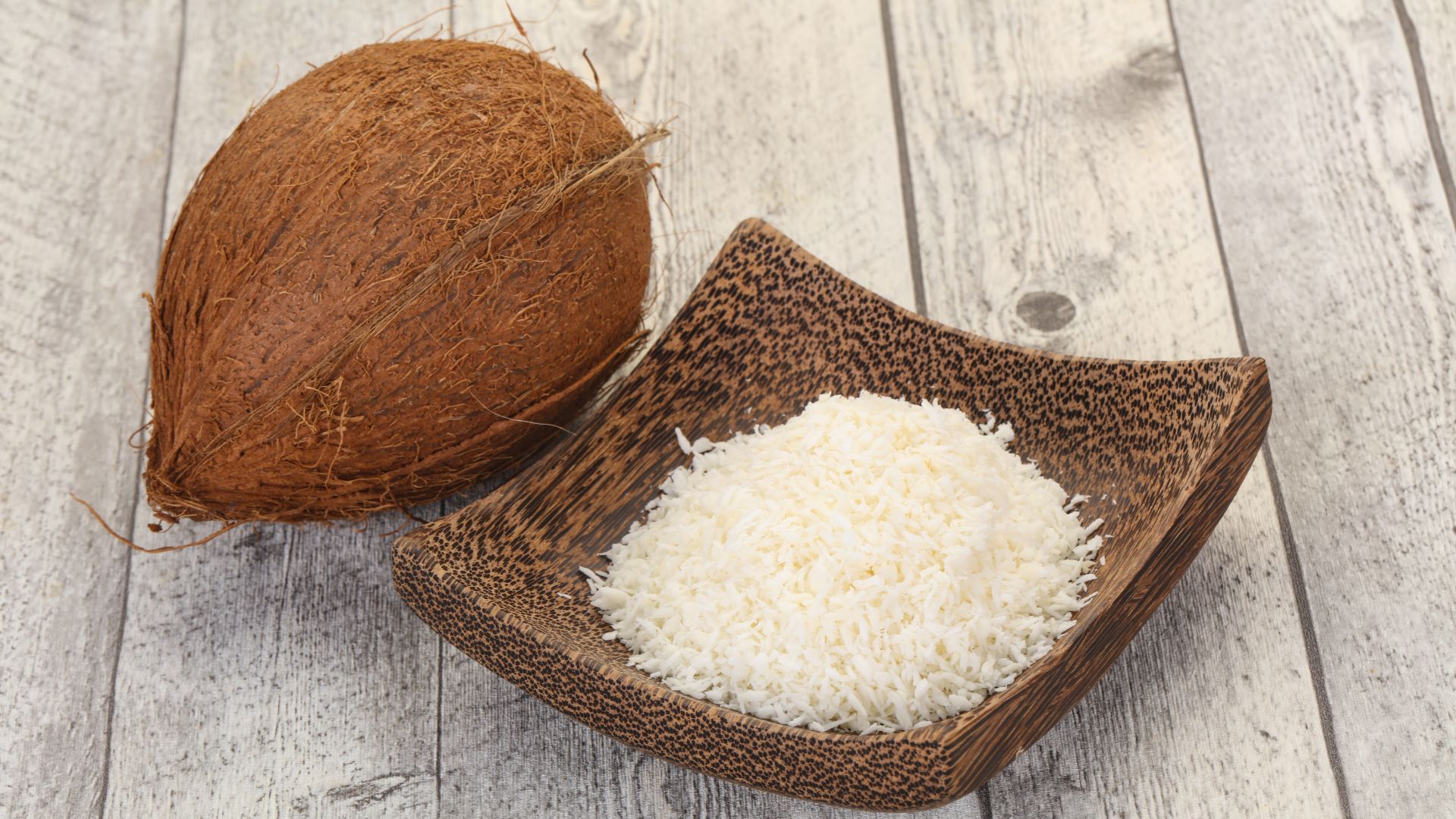 Un bol de noix de coco desséchée à côté d'une noix de coco fraîche
