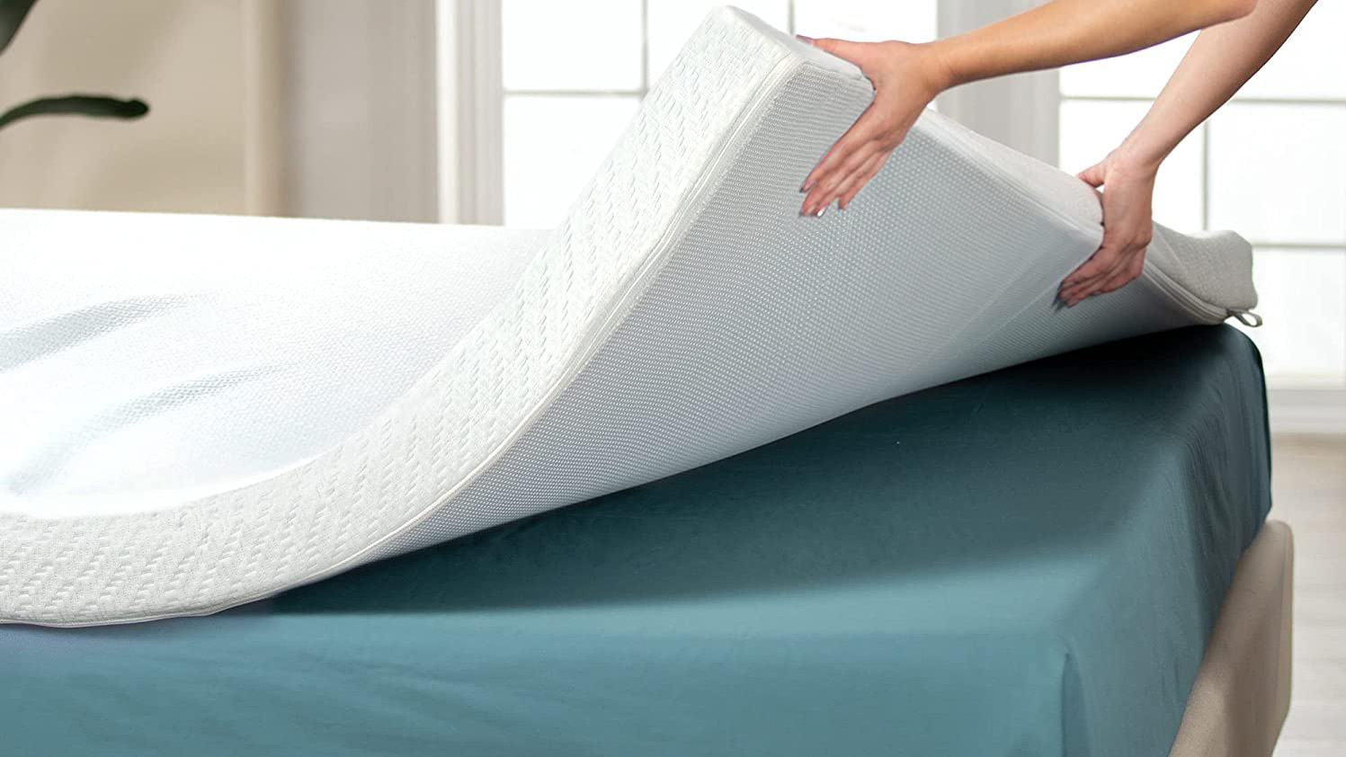 Une personne soulève le coin d'un haut matelas blanc épais sur un lit vêtu d'une feuille ajustée bleue