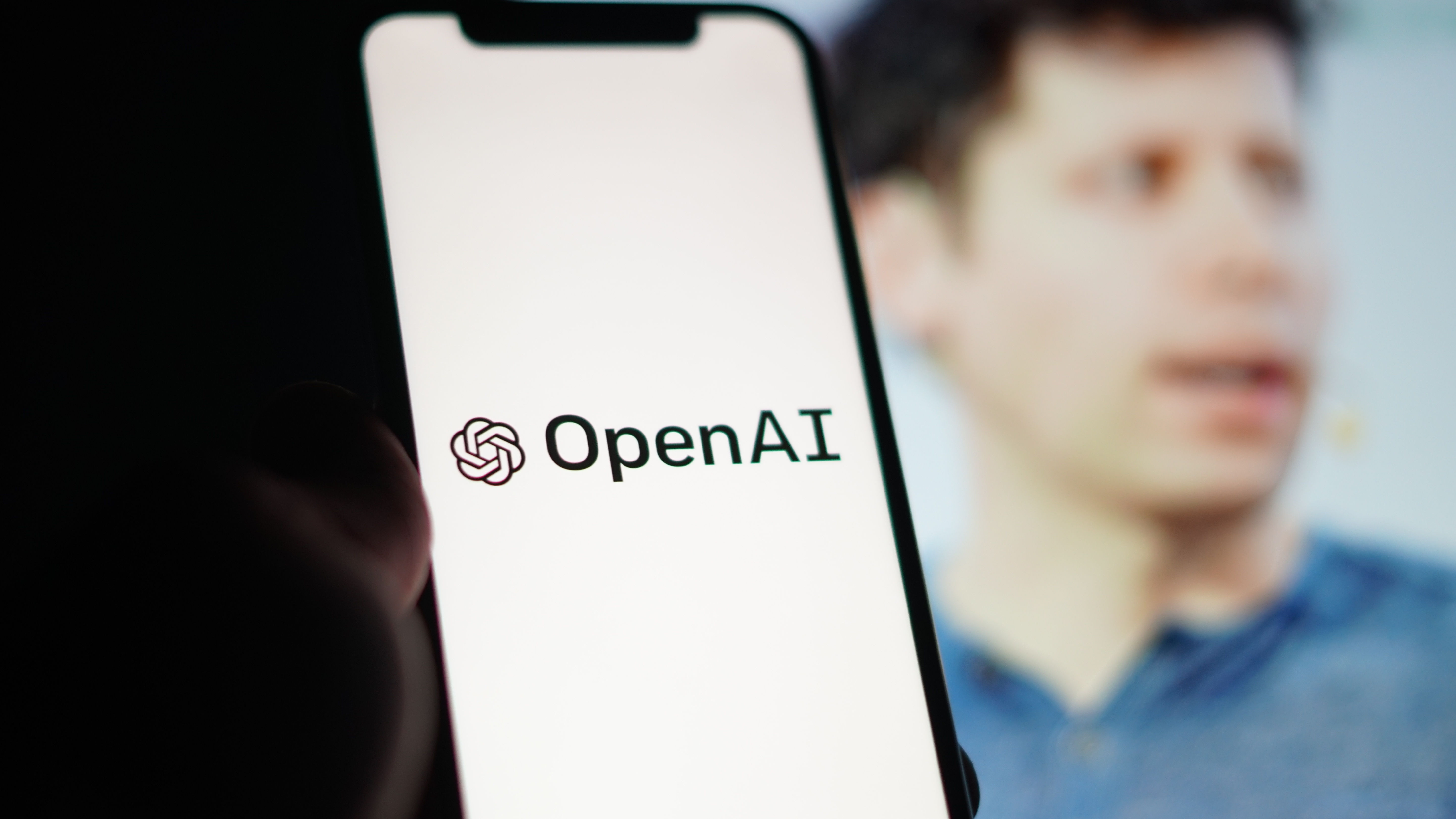 Openai Logo sur un écran de téléphone devant une image floue de Sam Altman