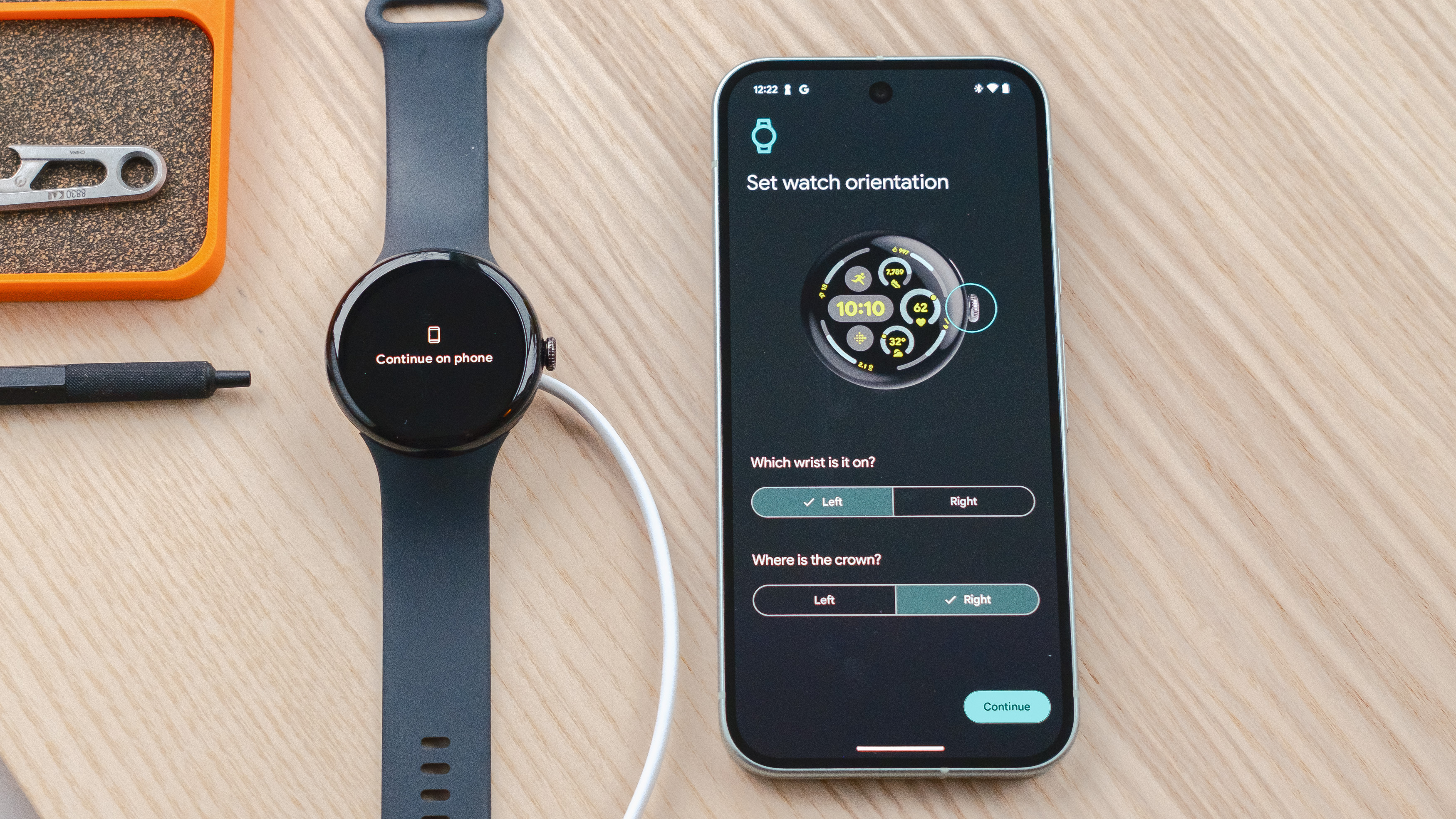 Google Pixel Watch 3 sur une table en bois à côté d'un smartphone Pixel 9 montrant un écran demandant aux utilisateurs de choisir leur préférence de poignet de montre intelligente et leur préférence d'orientation de la couronne