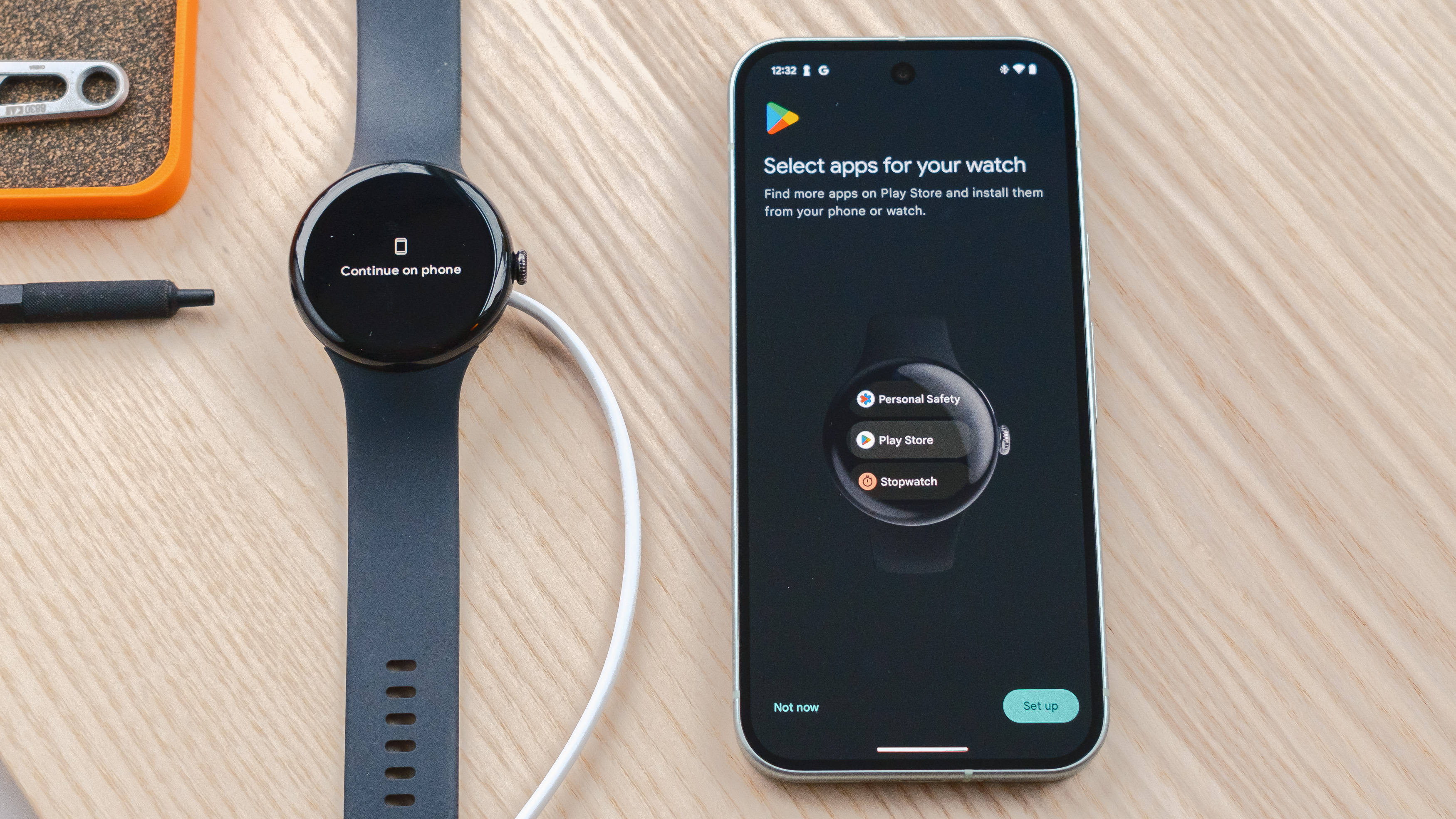 Google Pixel Watch 3 sur une table en bois à côté d'un smartphone Pixel 9 affichant un écran demandant aux utilisateurs de sélectionner les applications qu'ils souhaitent précharger sur leur montre pendant le processus de configuration