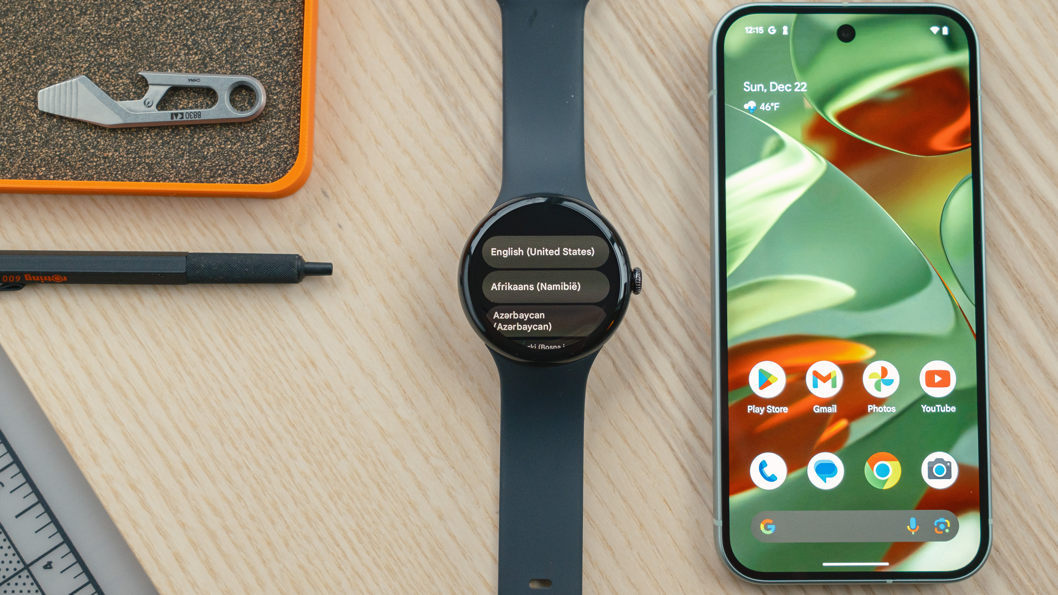 Google Pixel Watch sur un bureau en bois à côté d'un smartphone affichant un écran avec des options de sélection de langue