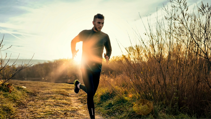 Un homme portant du lycra noir qui traverse un champ avec du soleil levant brillant derrière lui