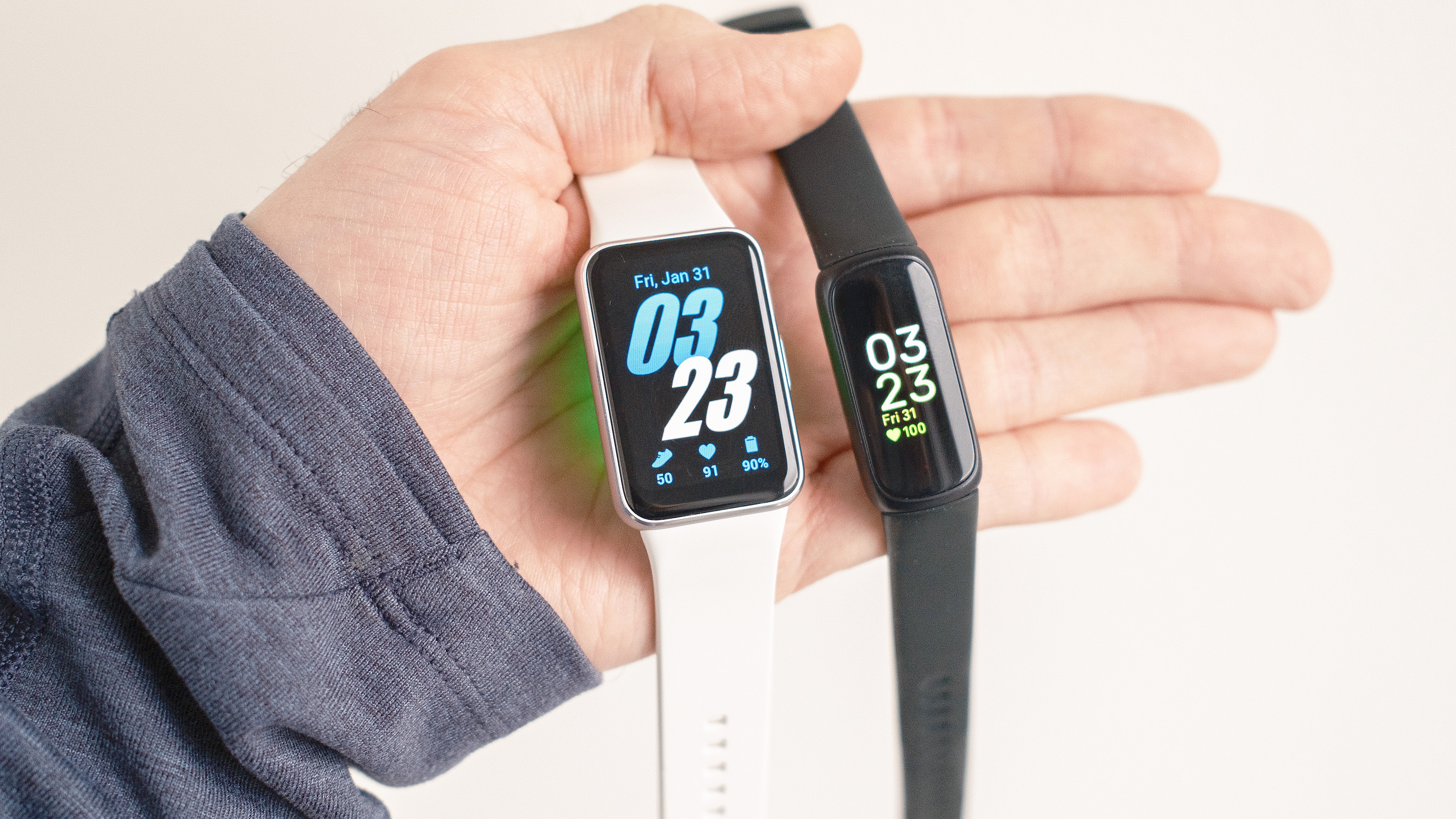 Gros plan du Samsung Galaxy Fit3 à côté du Fitbit Inspire 3 dans la main d'un utilisateur