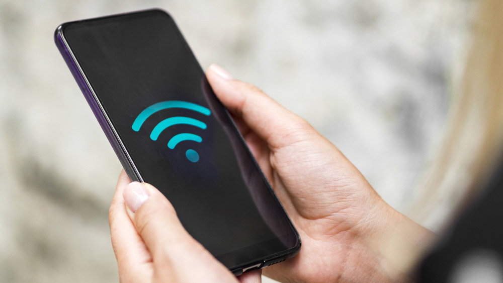 Le symbole Wi-Fi affiché sur l’écran d’un smartphone tenu entre les mains d’une personne.