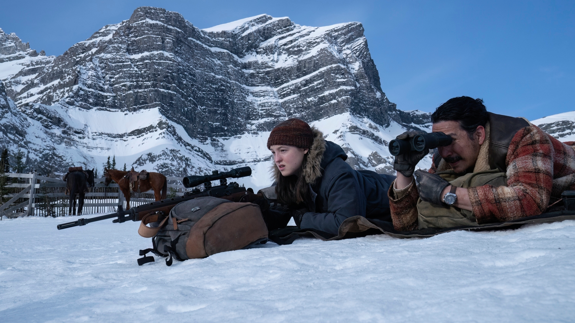 Ellie (Bella Ramsey) armé d'un fusil de sniper et de Tommy (Gabriel Luna) allongé dans la neige