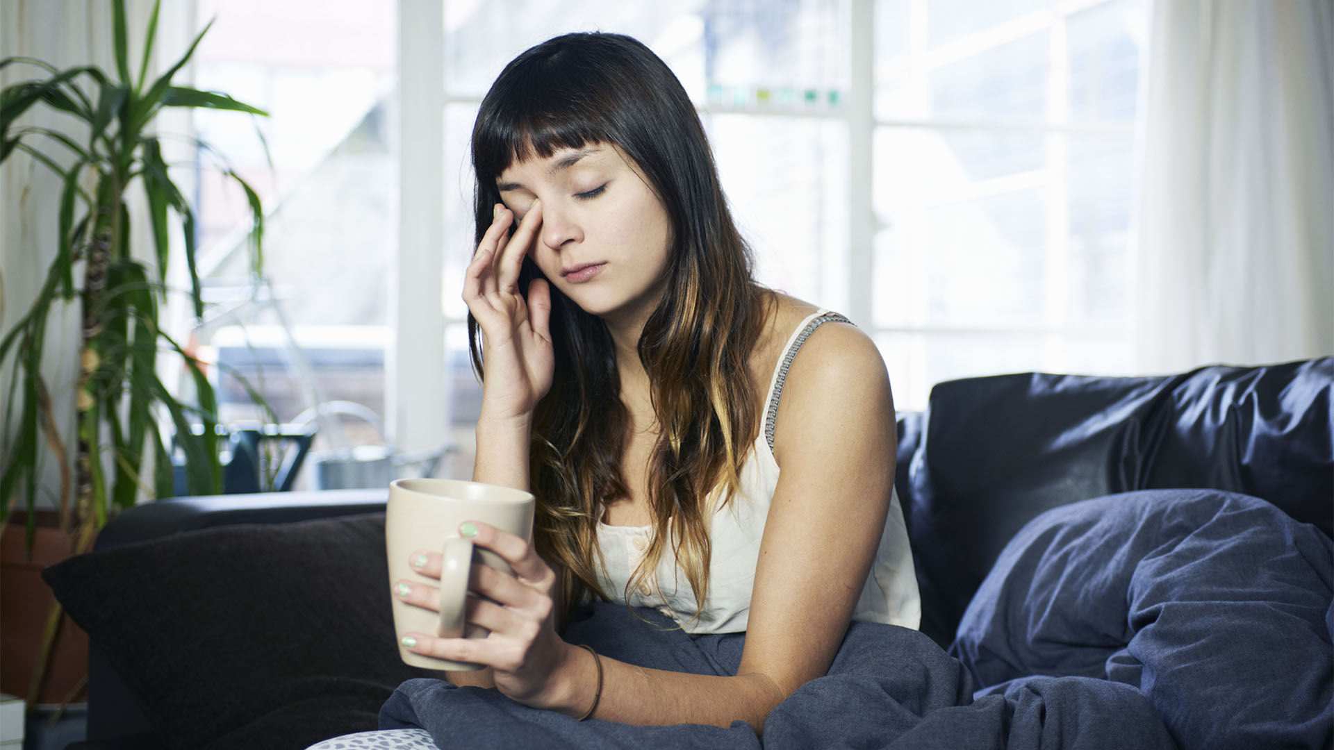 Une femme s'assoit dans son lit en l'air fatigué en tenant une tasse de café