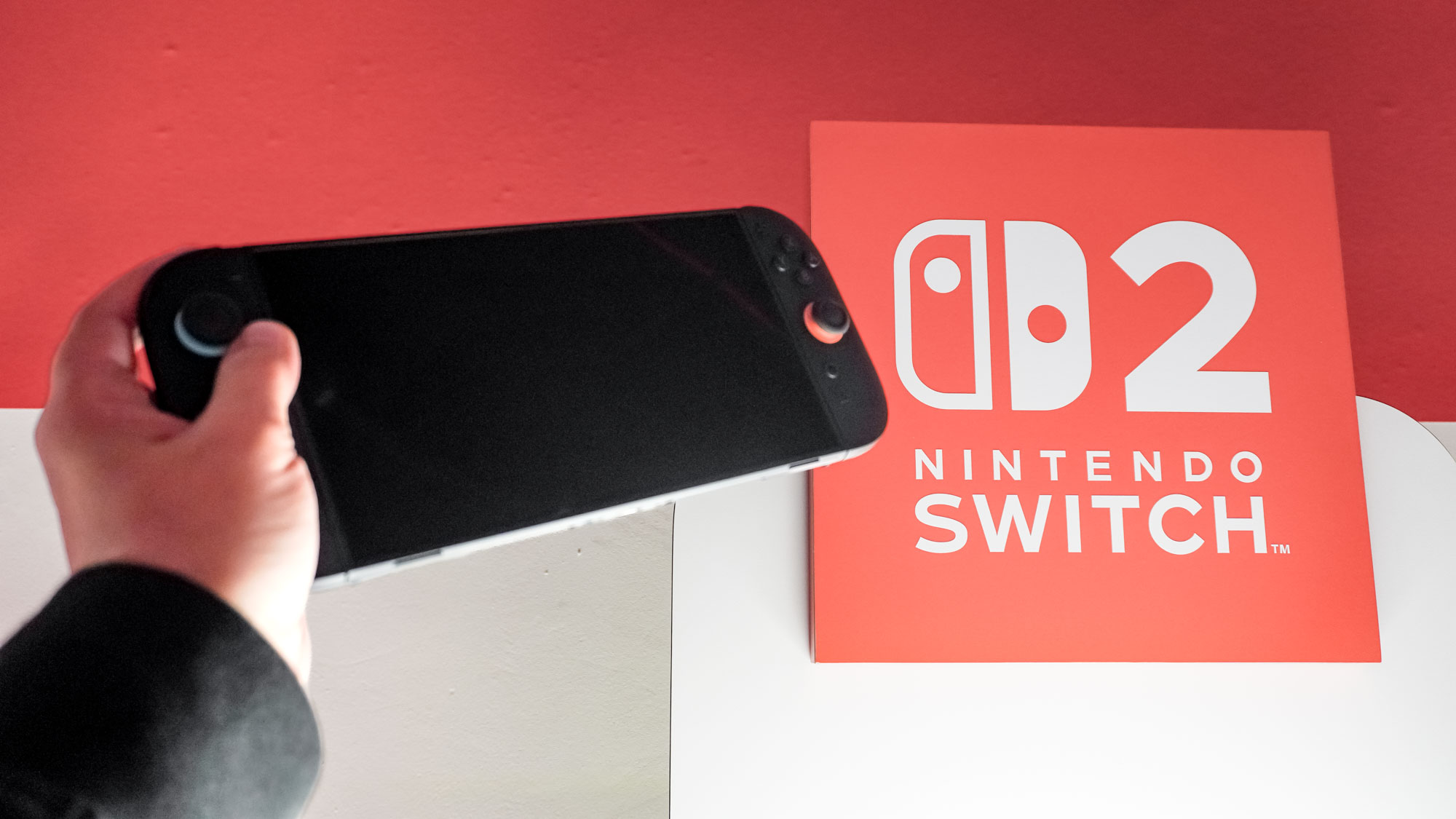 Une console Nintendo Switch 2 en main à côté du logo Nintendo Switch 2