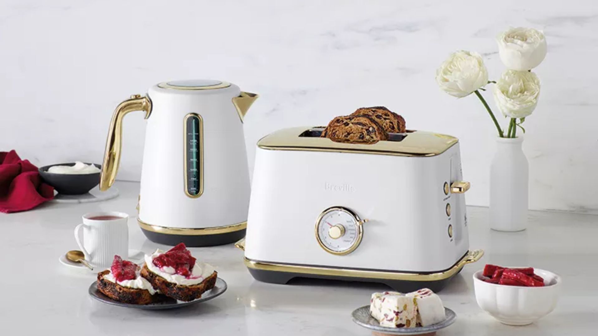 Les appareils électroménagers de la cuisine en laiton de Breville se gèrent sur un plan de travail de cuisine avec des friandises et des fleurs autour