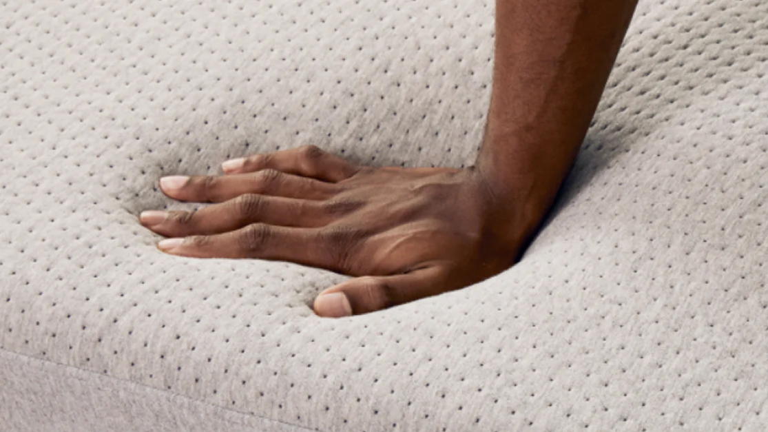 Un gros plan d'une main pressant dans la surface du matelas Casper Cloud One, sentant les mousser en peluche en dessous
