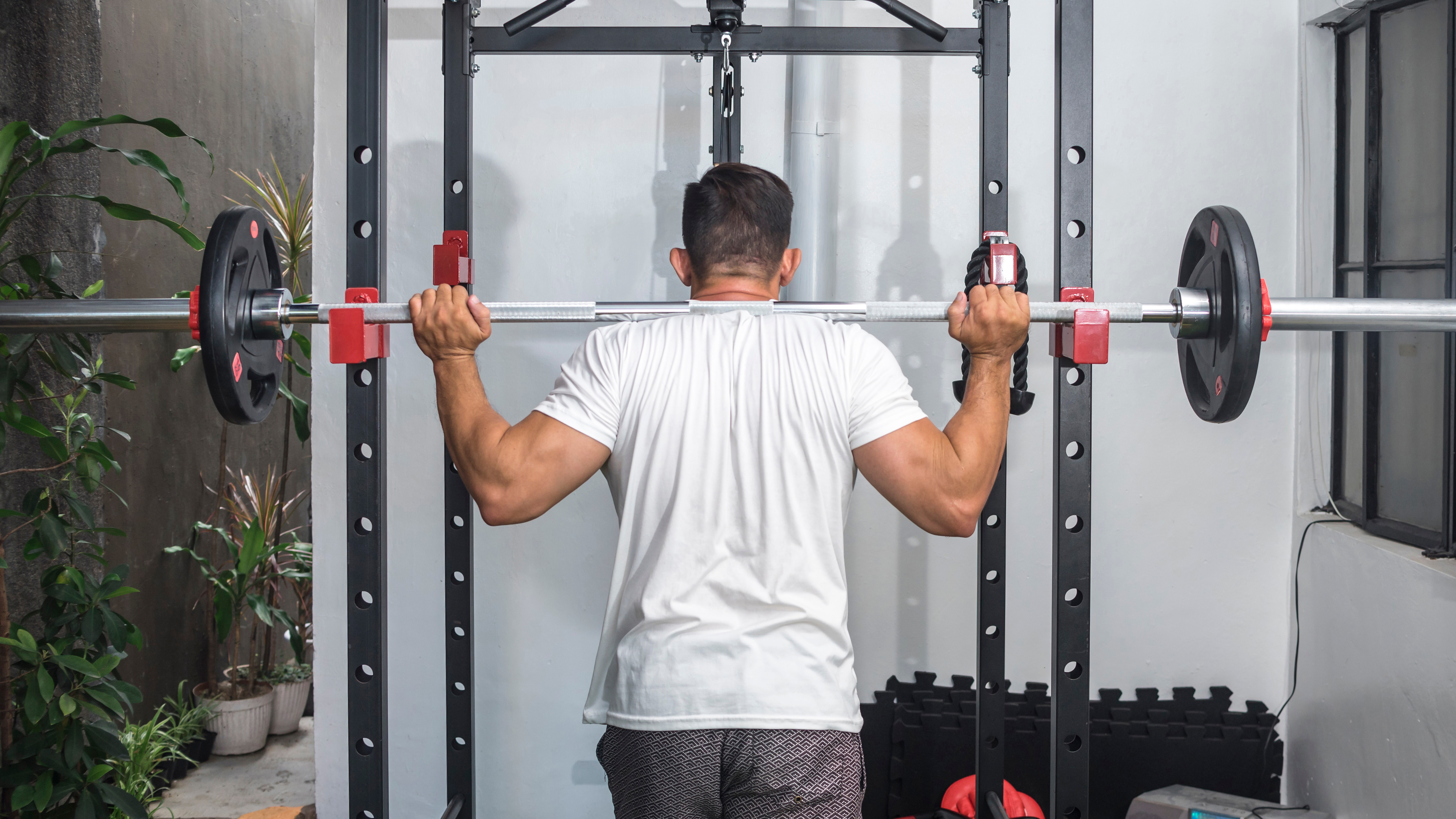 Un homme s'installant sur une barre de rack de squat plaçant sur le dos avec des poids chargés sur des haltères