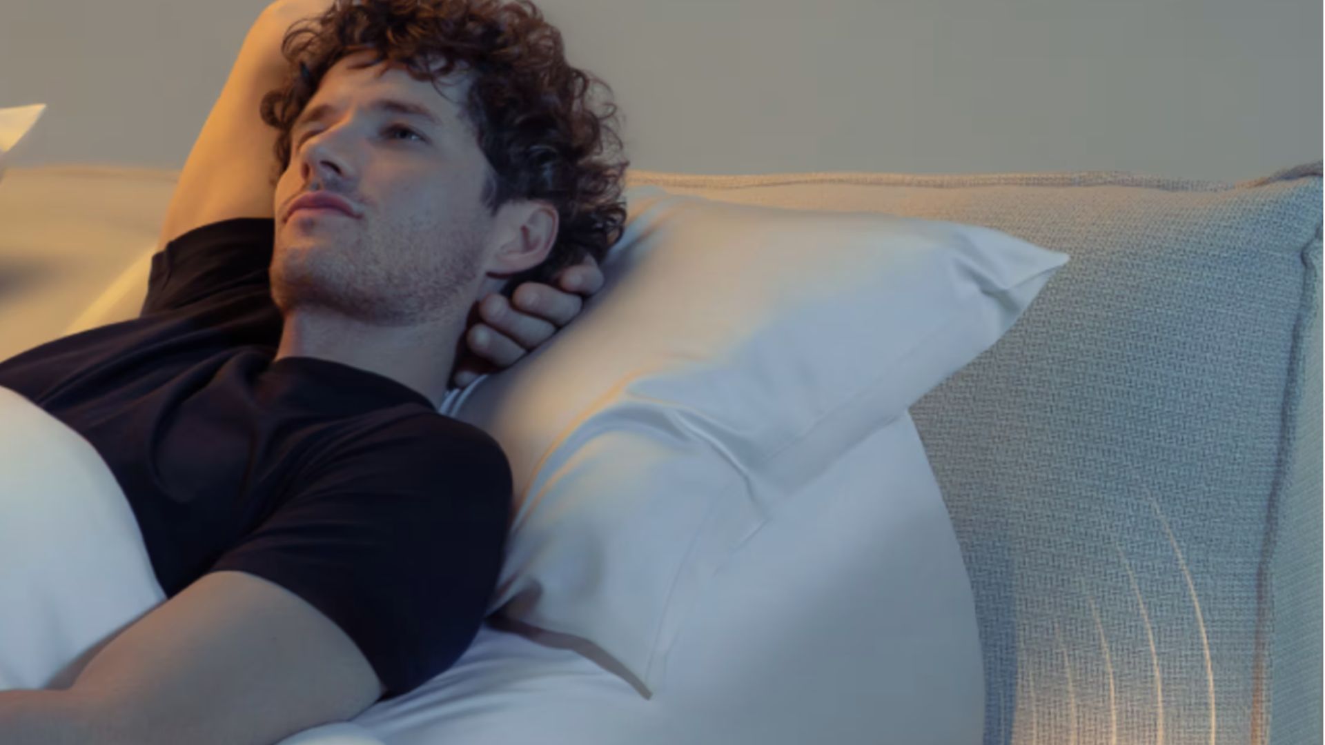 Un homme allongé sur le dos dans son lit avec un bras étiré derrière la tête sur huit dorsion Pod 5 Ultra