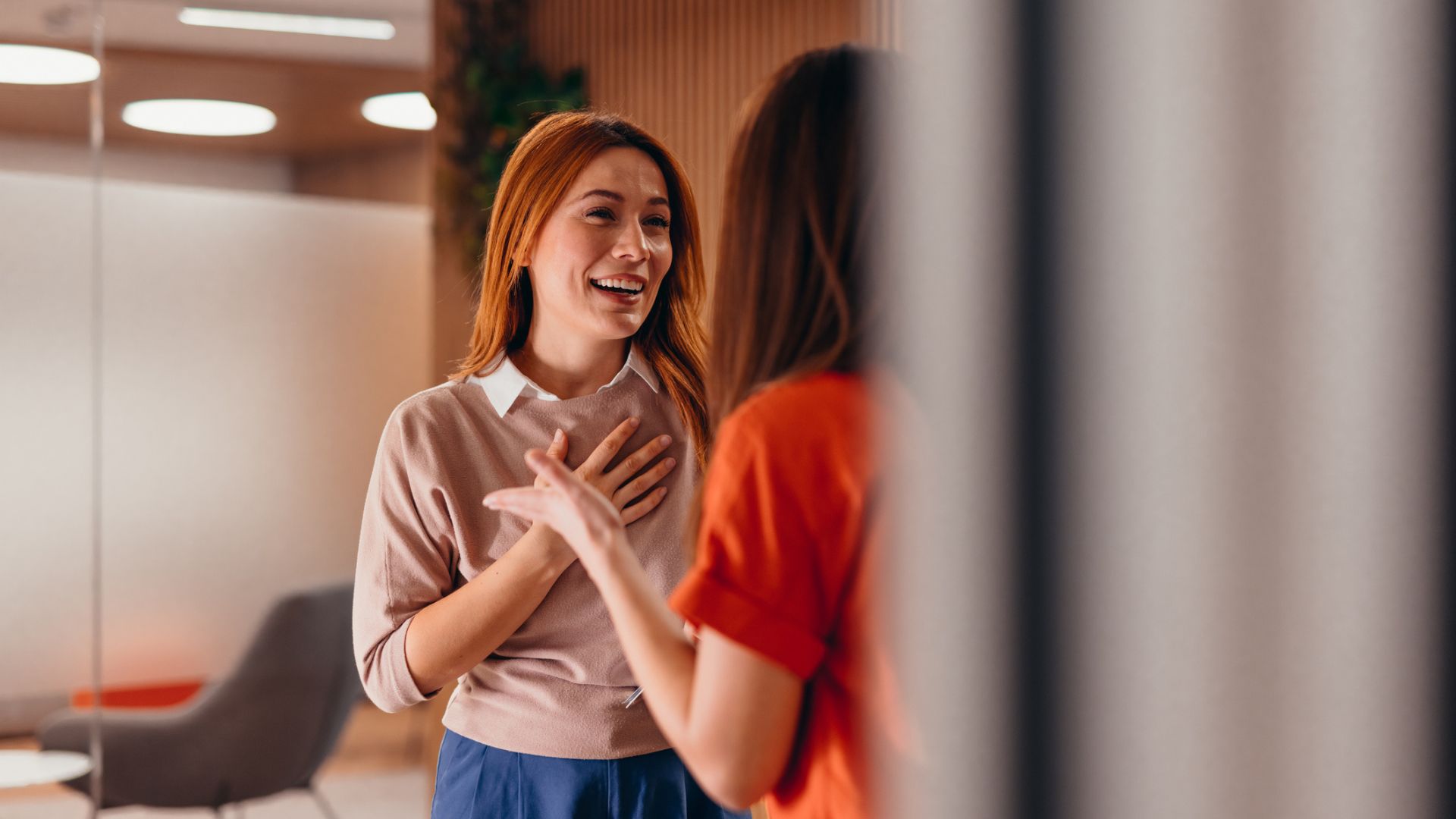 Une femme aux cheveux roux souriant et riant tout en socialisant avec son collègue