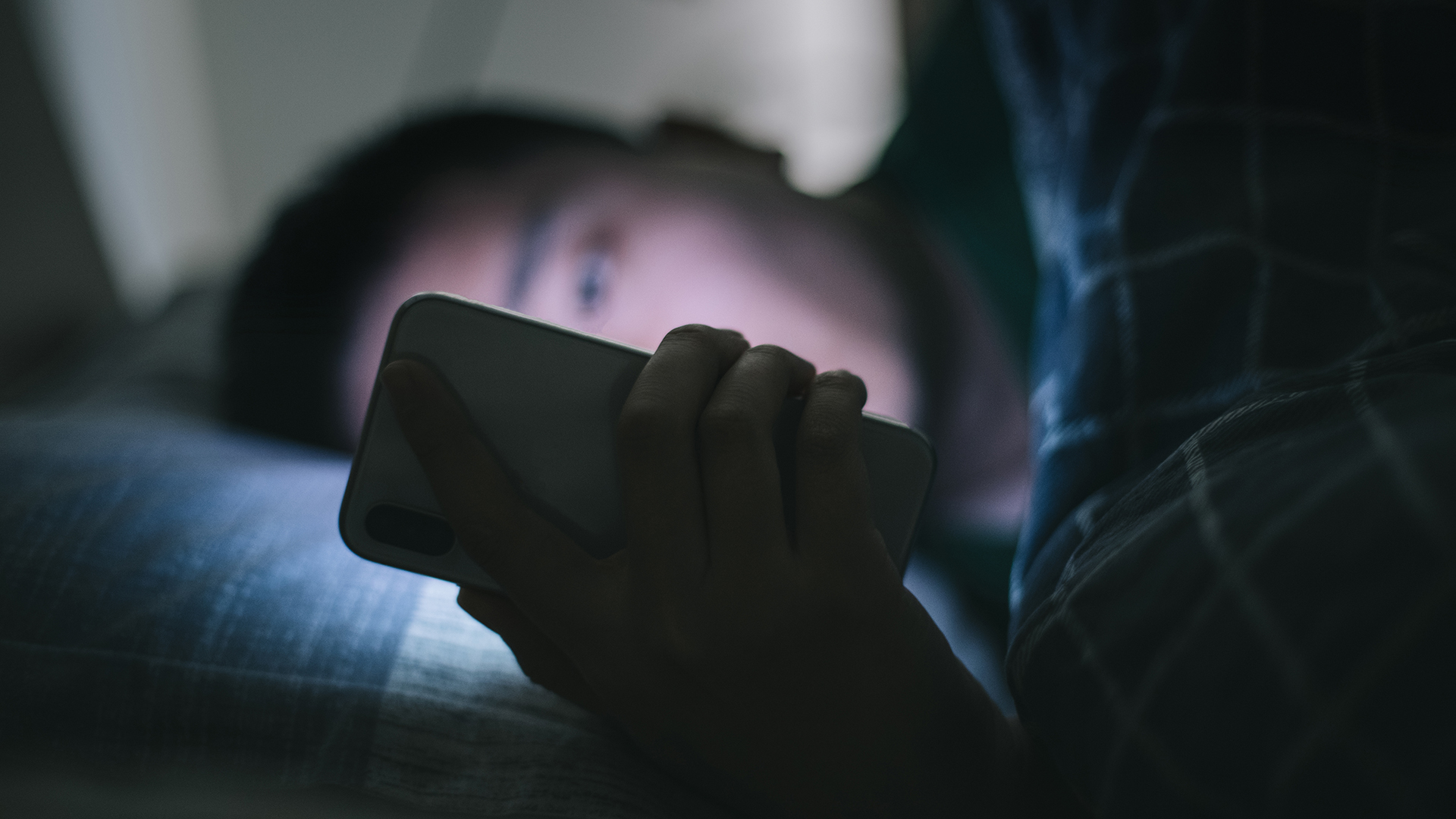Un homme est allongé dans son lit en regardant son téléphone, qui brille une lumière vive dans son visage