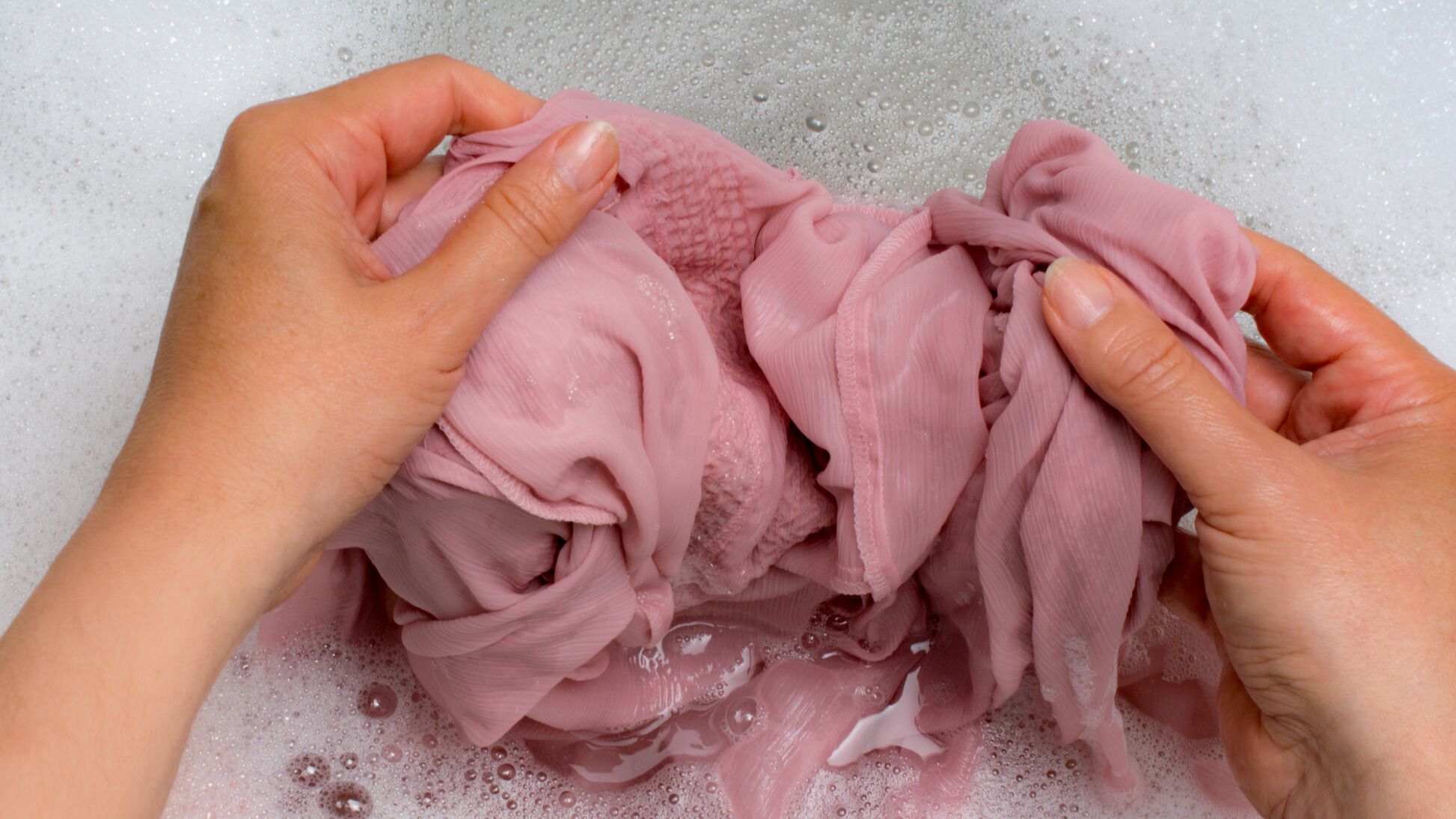 Lavage des mains dans une taie d'oreiller en soie rose dans l'eau savonneuse