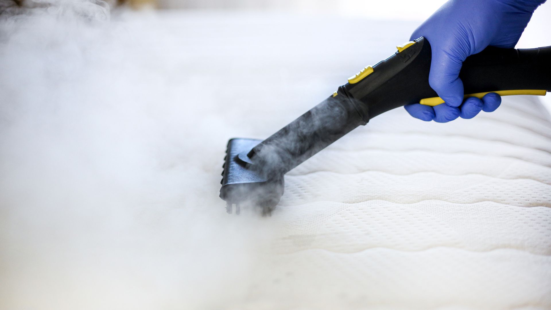 Un nettoyeur à vapeur dépassant un matelas avec un nuage de vapeur dessus
