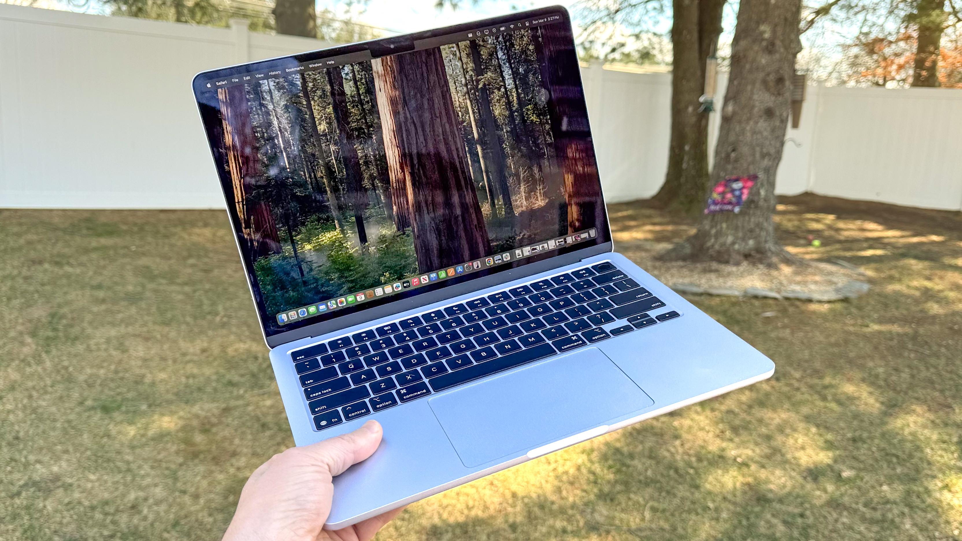 Personne tenant le MacBook Air M4 13 pouces à l'extérieur, au-dessus de l'herbe, dans un jardin ombragé