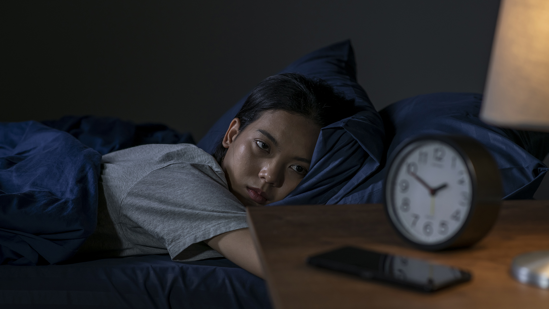 Une personne est allongée au lit au milieu de la nuit, incapable de dormir et regardant l'horloge