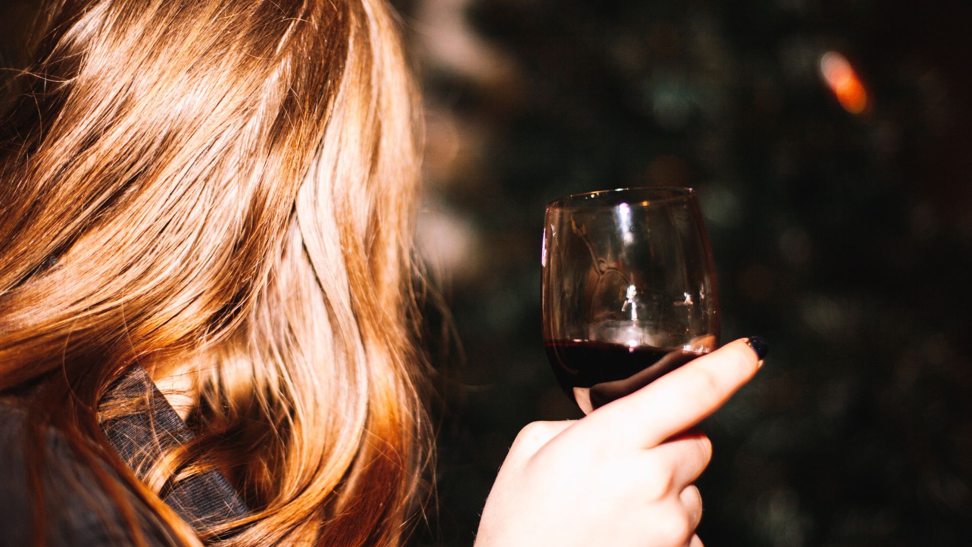 Une femme tient un verre de vin la nuit, elle fait face à la caméra.