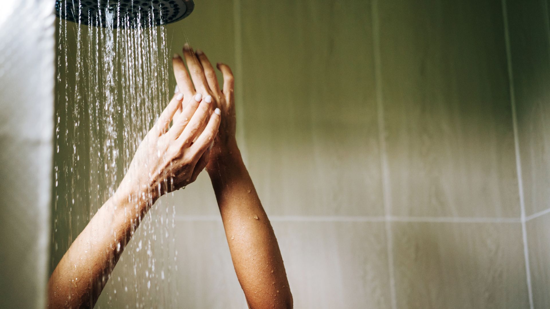 Une personne se tient sous la douche, les bras levés. La salle de bains présente des panneaux muraux imitation bois clair.
