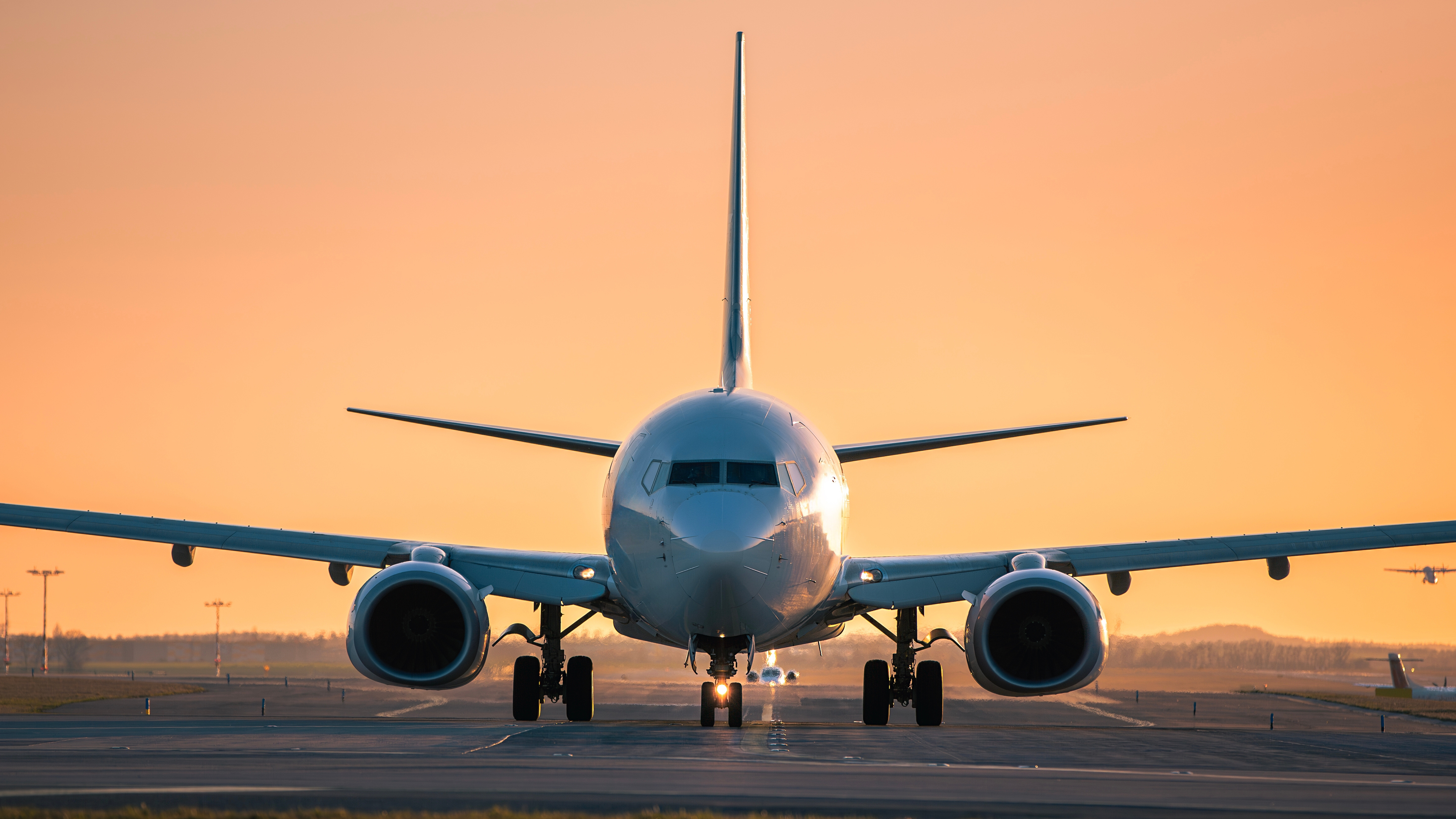 Trafic à l'aéroport au coucher du soleil doré. Vue de face d'un avion au roulage tandis que d'autres décollent de la piste