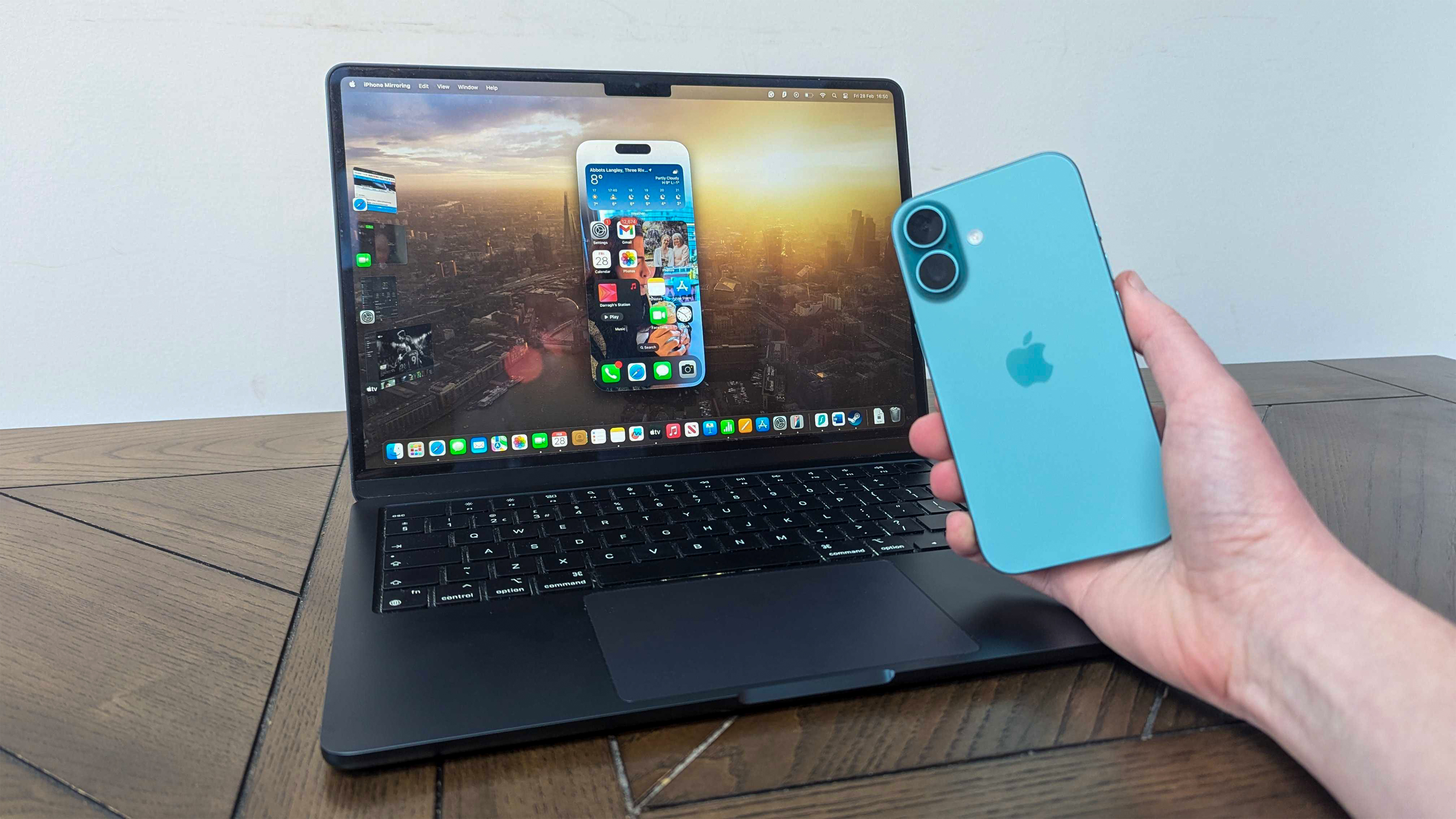 Un iPhone 16 à la main devant un MacBook Air M3 13 pouces sur table