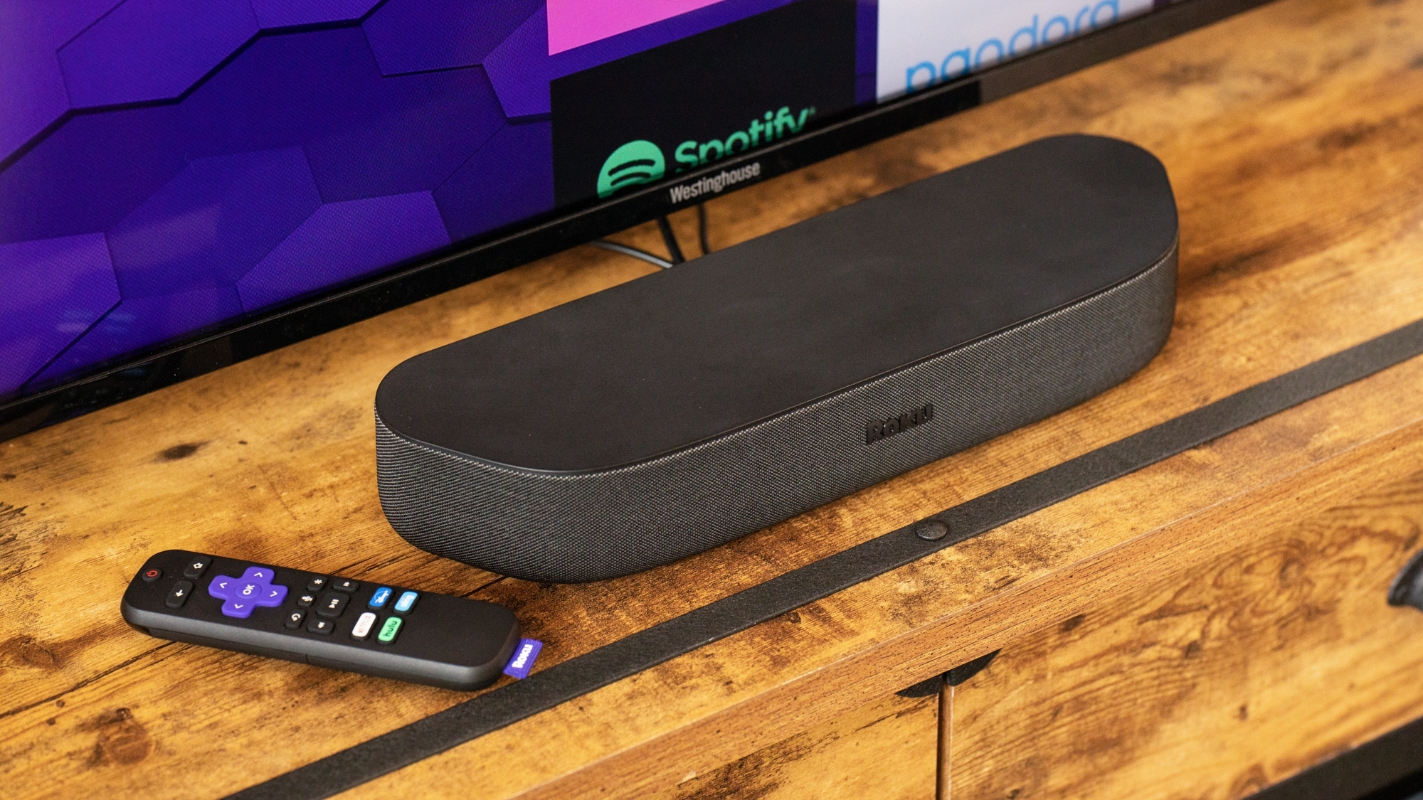 Roku Streambar sur un comptoir devant un téléviseur à côté d'une télécommande Roku