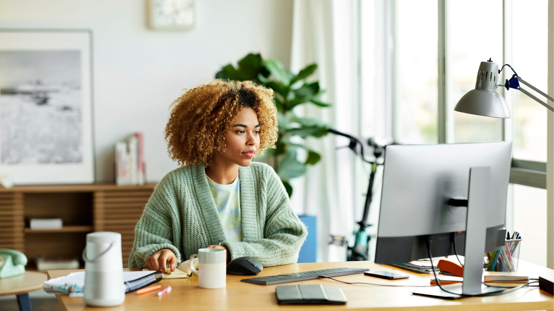Une femme est assise à un bureau dans une pièce bien éclairée et regarde un écran d’ordinateur.