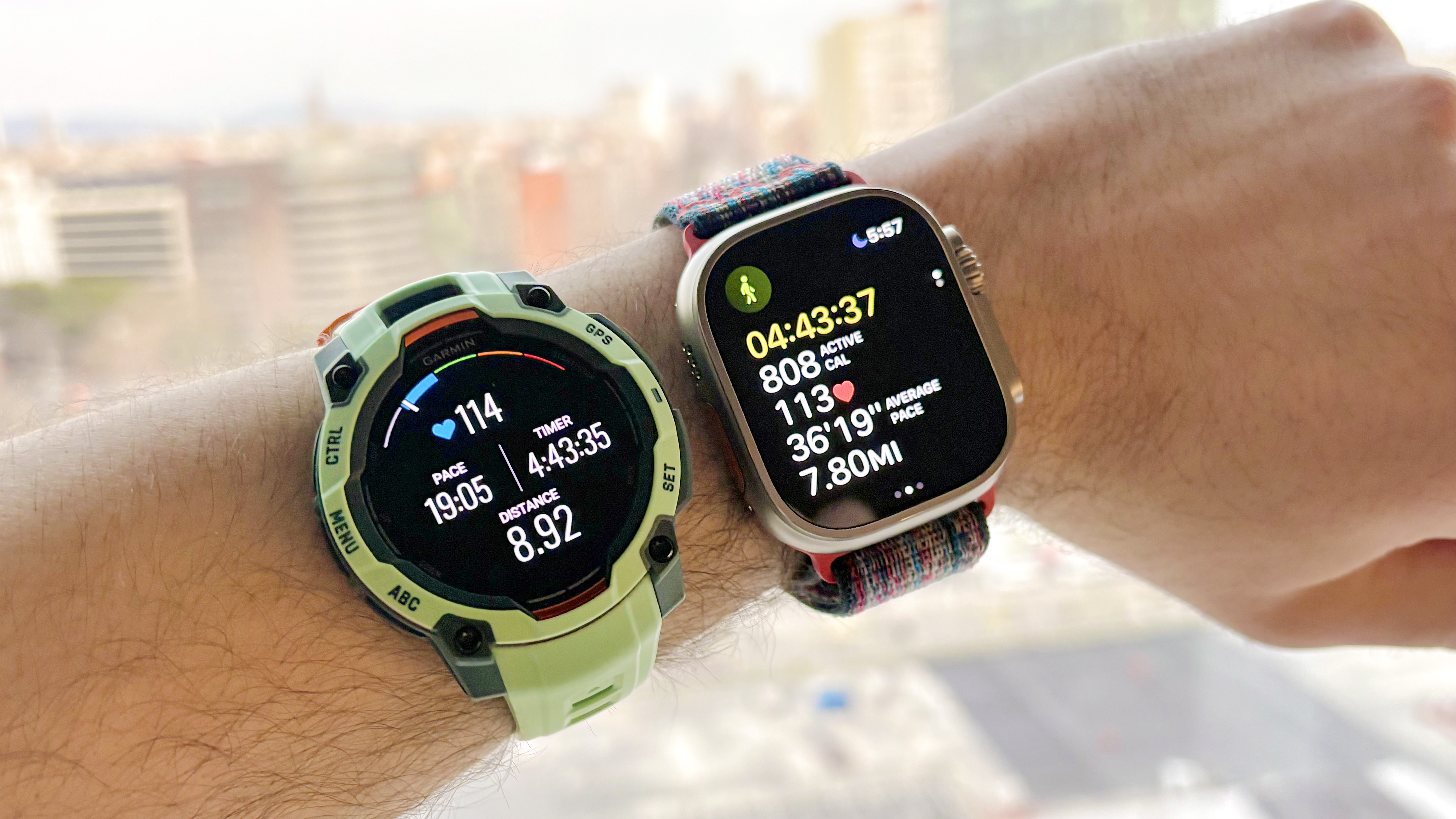 Gros plan de la Garmin Instinct 3 à côté de l'Apple Watch Ultra 3 avec l'horizon de Barcelone au loin