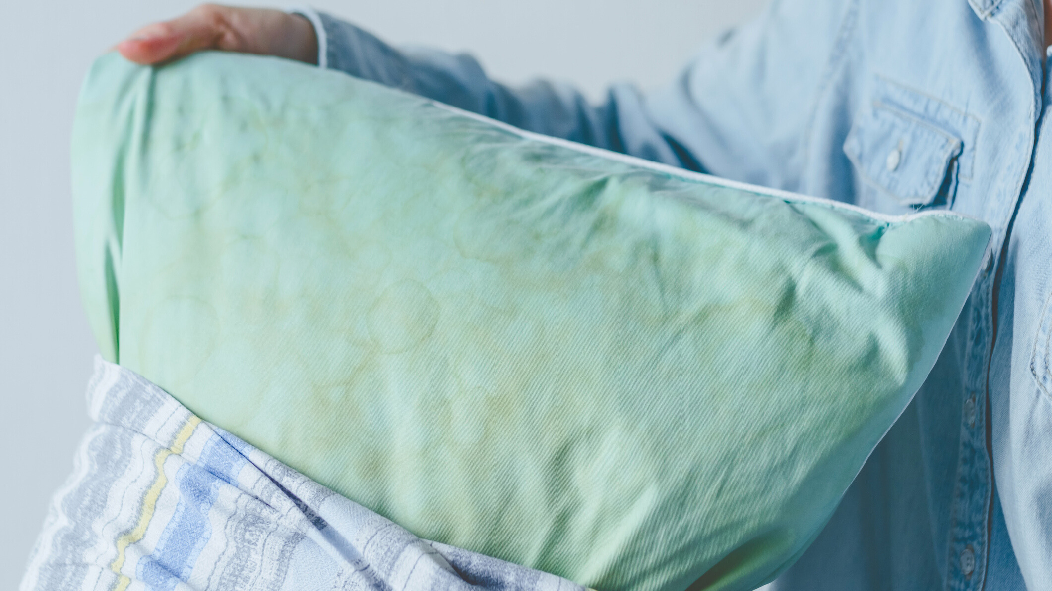 Une personne prenant un oreiller taché de bleu avec du jaune rapiécé sur une taie d'oreiller imprimée