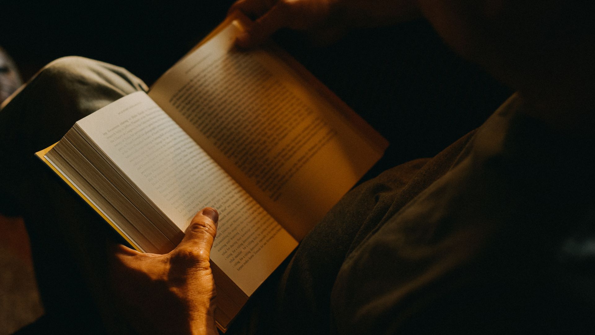 Une personne lisant un livre dans une pièce faiblement éclairée.