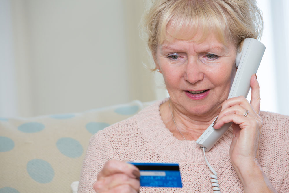 Une femme âgée inquiète lit la carte de paiement tout en tenant le téléphone.