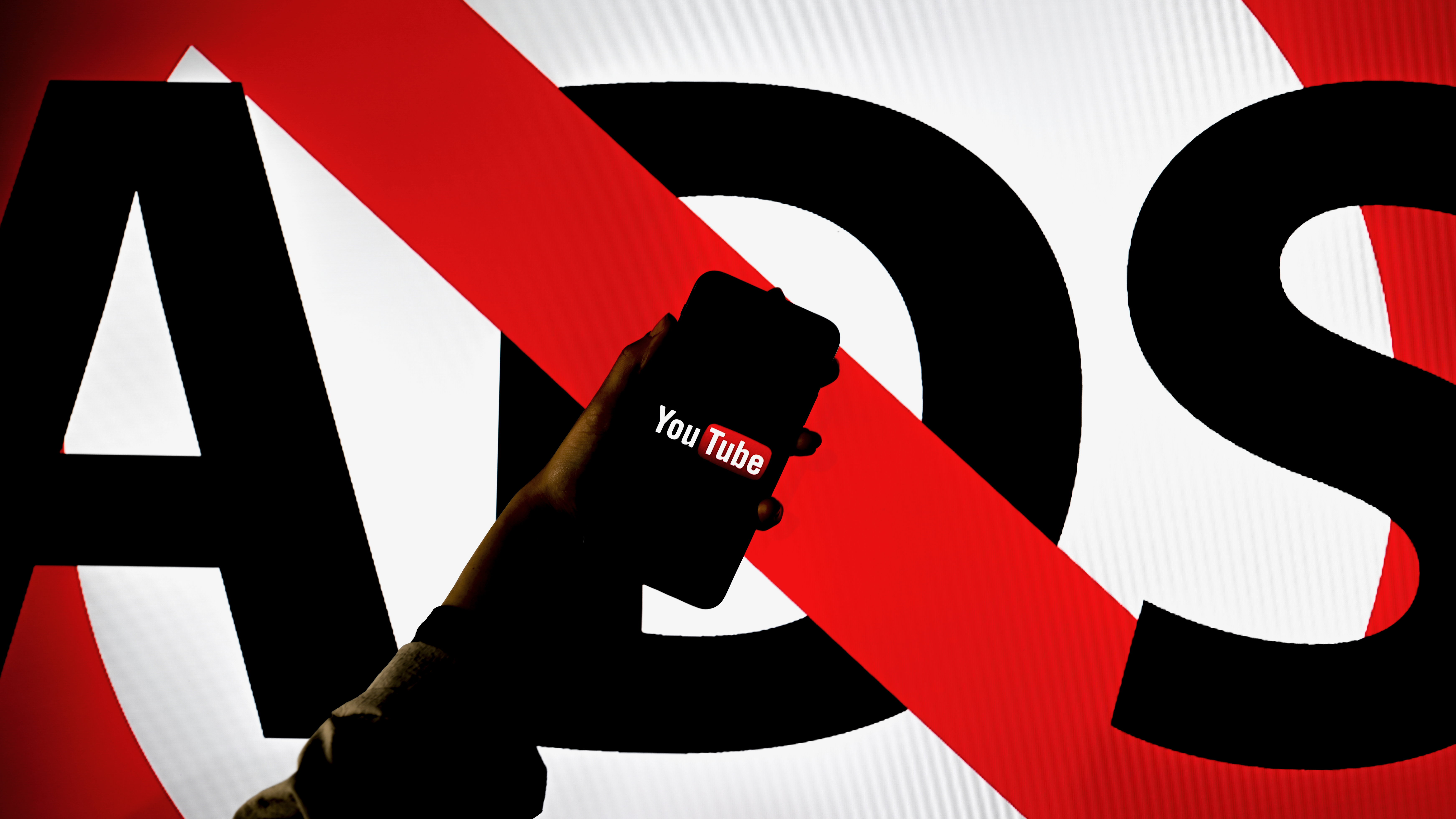 Un grand panneau avec le mot « ADS » barré, avec un smartphone affichant l'application YouTube devant lui.