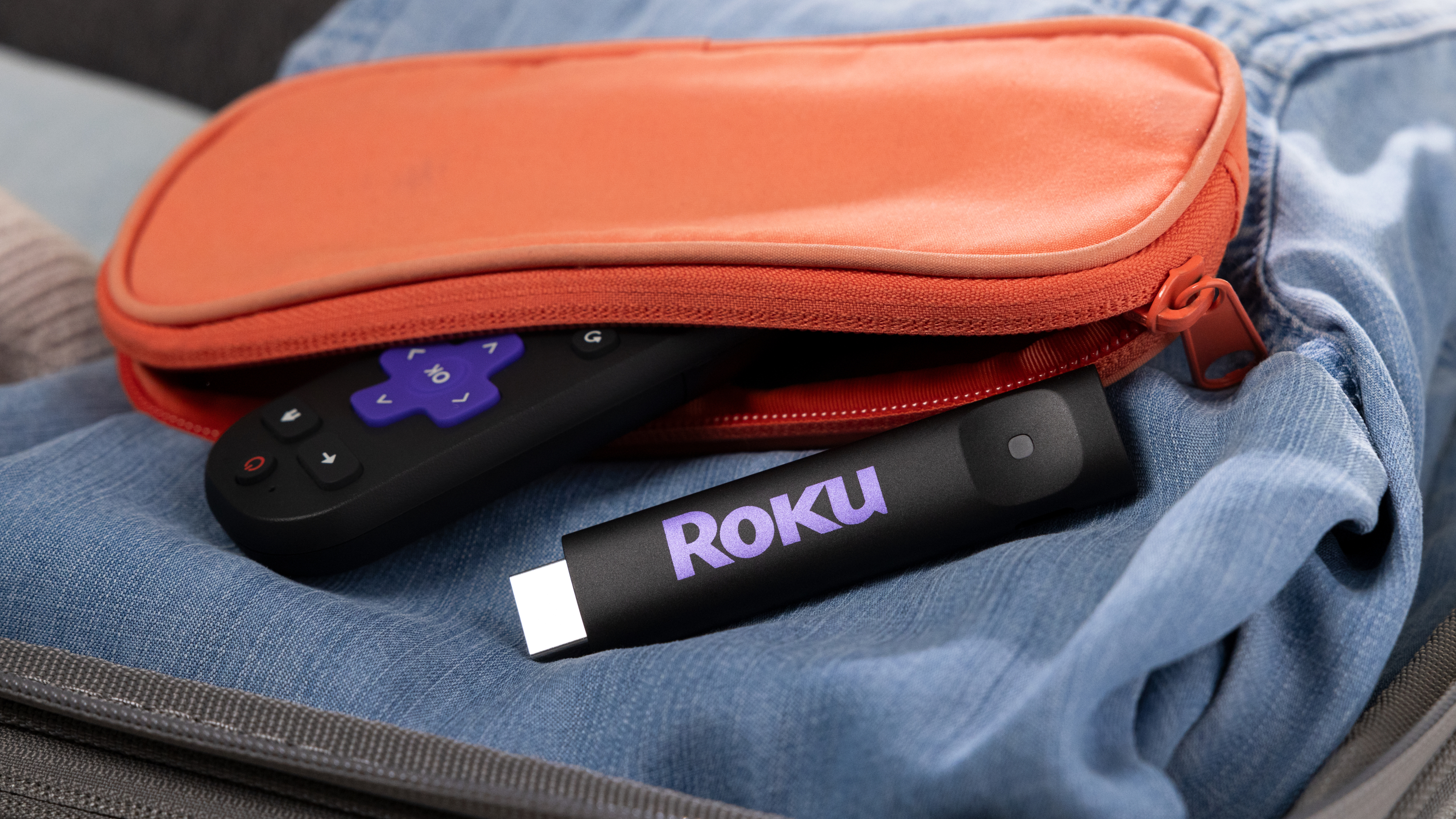 Le Roku Streaming Stick 2025 et une télécommande Roku sortant d'une pochette de couleur orange, tous posés sur un denim plié