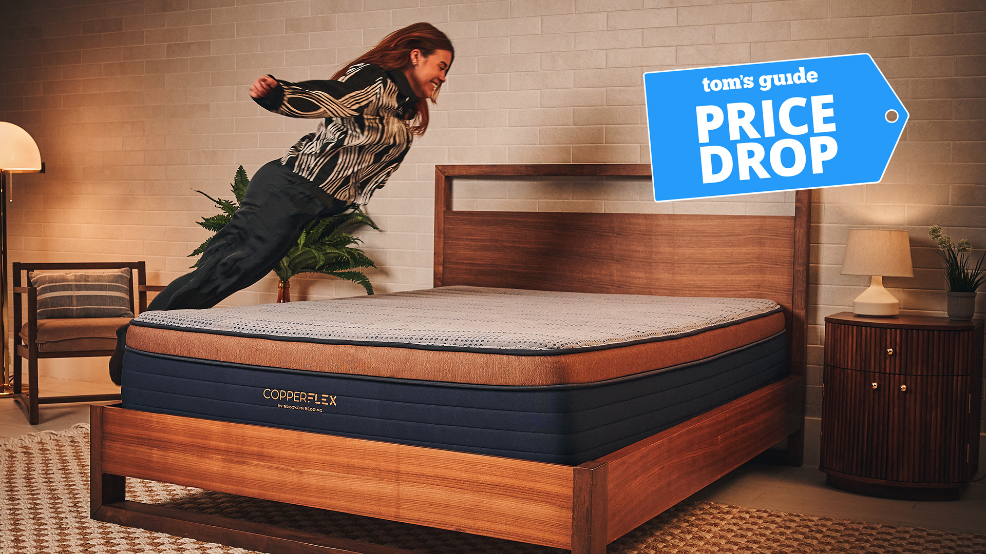 La testeuse de matelas Eve Davies saute sur le matelas Brooklyn Bedding CopperFlex Pro dans une pièce chaleureusement éclairée. Dans le coin supérieur droit se trouve un graphique des offres de baisse de prix de Tom's Guide.