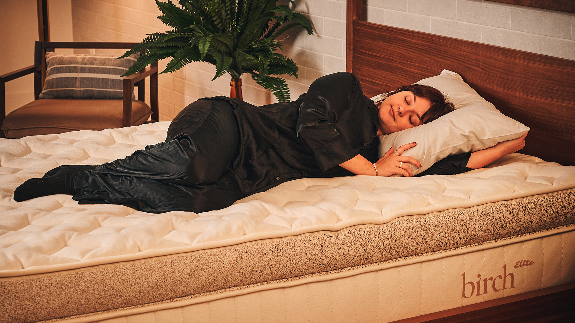 Notre testeur de matelas Lauren Jeffries s'allonge sur le matelas Birt Elite Natural en position de sommeil latérale. Le matelas est sur un cadre de lit en bois dans une pièce décorée. Elle utilise un oreiller haut pour amortir sa tête, son cou et ses épaules.