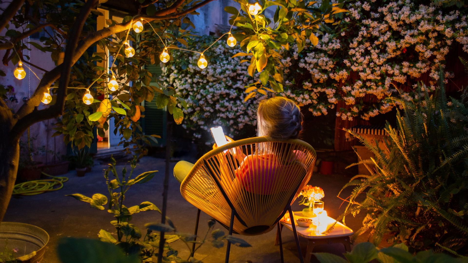 Une femme lisant son téléphone sur une chaise dans son jardin, au crépuscule