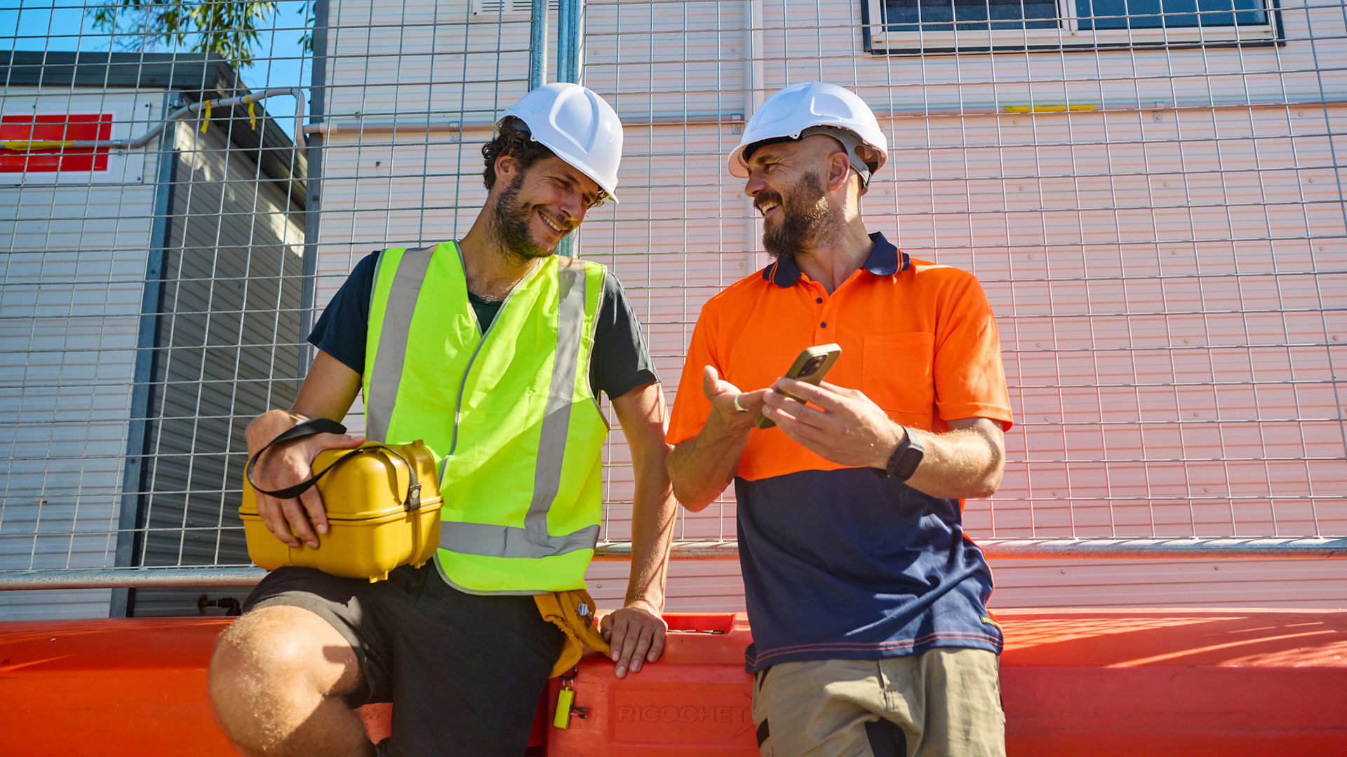 Deux commerçants en équipement haute visibilité regardant un téléphone portable et souriant