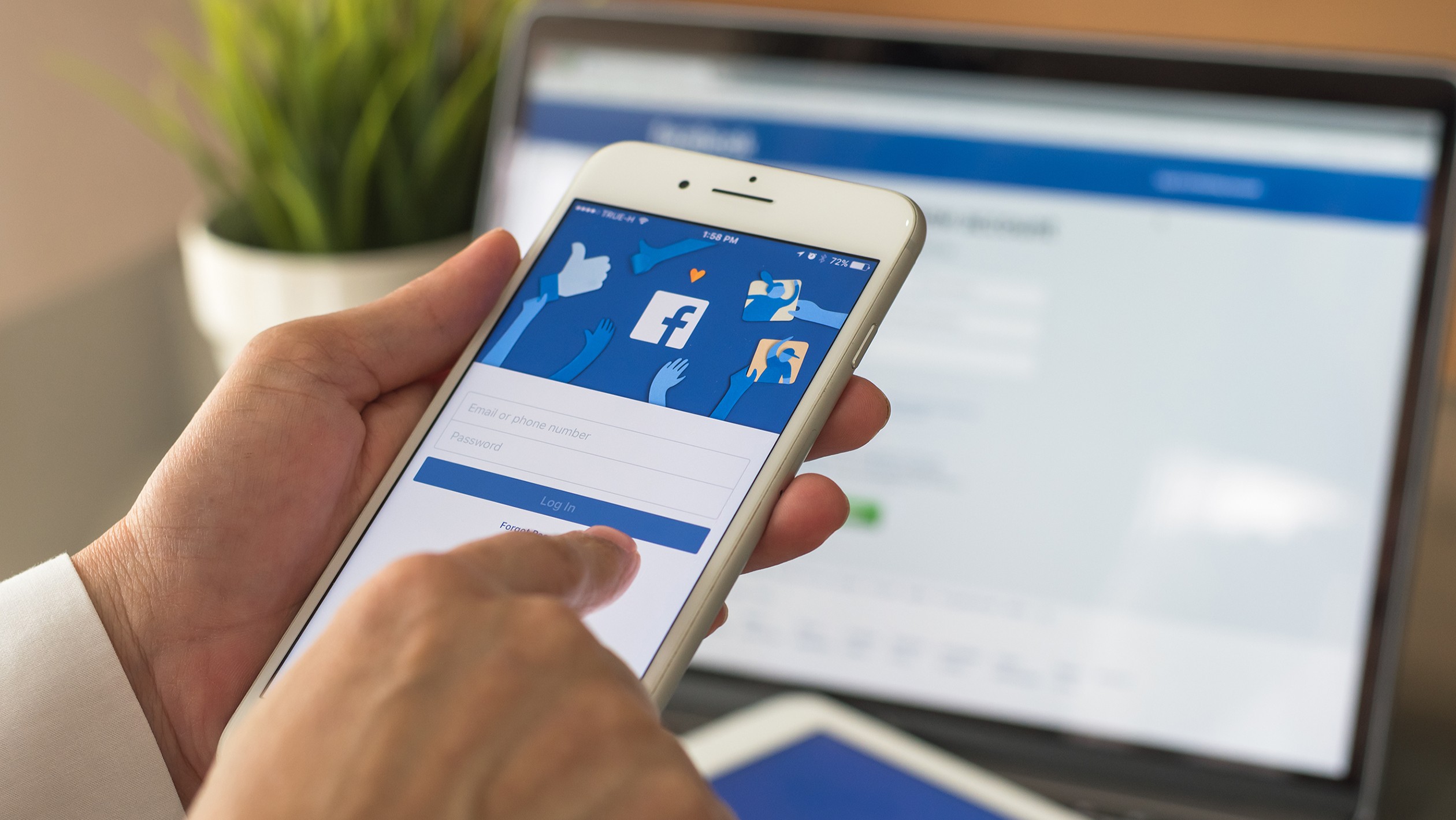 Une personne se connectant à Facebook sur son téléphone et le site étant également ouvert sur un ordinateur portable en arrière-plan