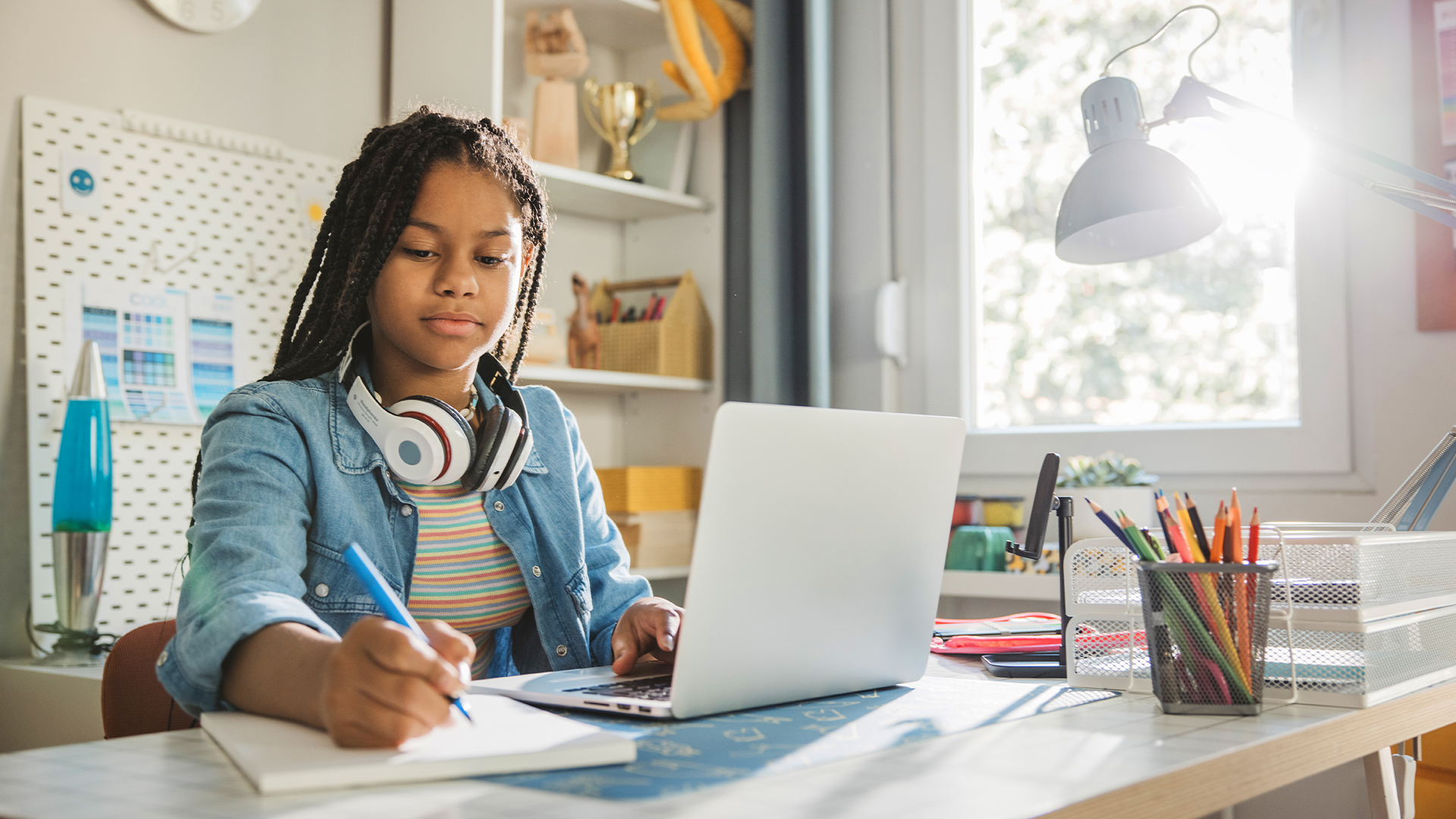 Une jeune fille fait ses devoirs, écrit dans son bloc-notes tout en travaillant sur son ordinateur portable
