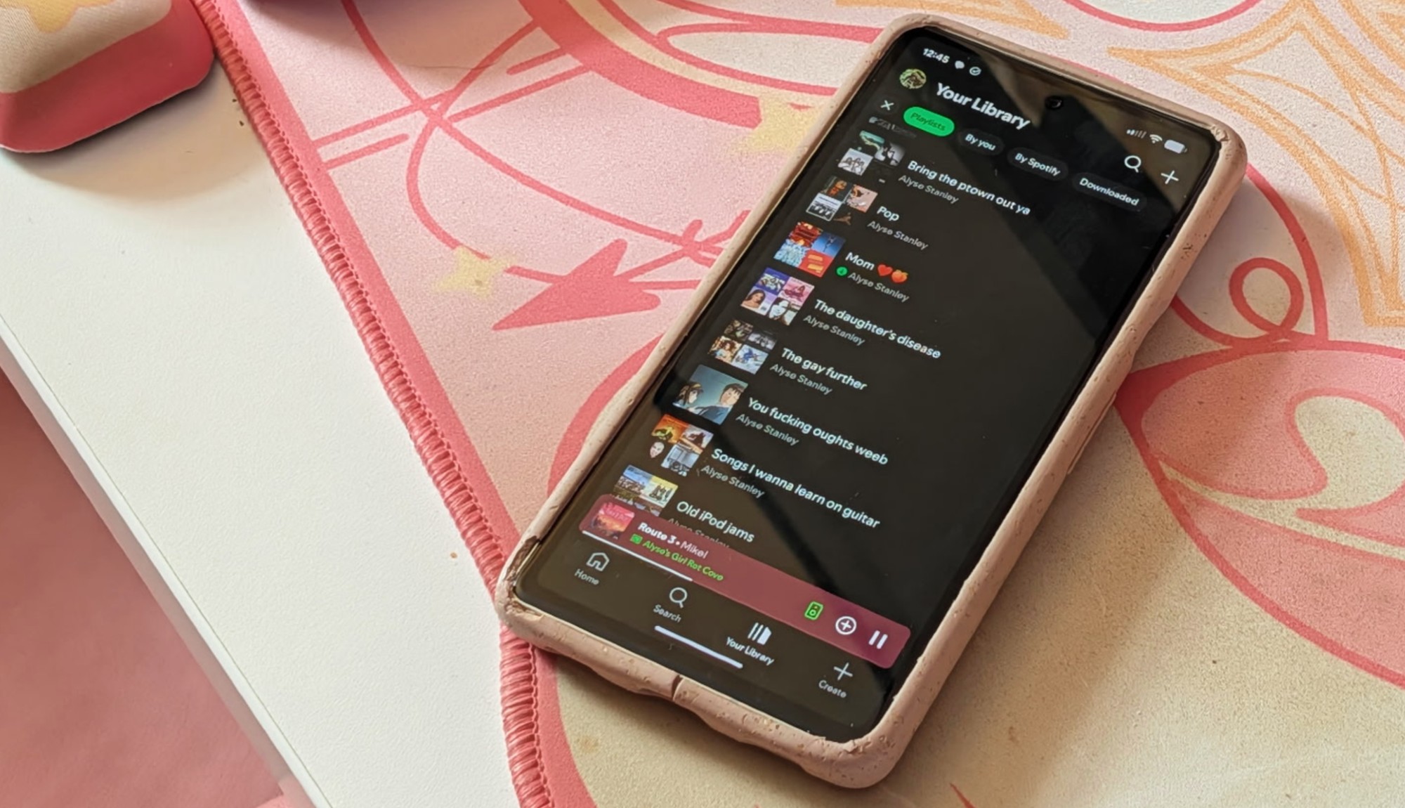 Une photo d'un Pixel 7a avec l'application Spotify affichée sur un sous-main rose.