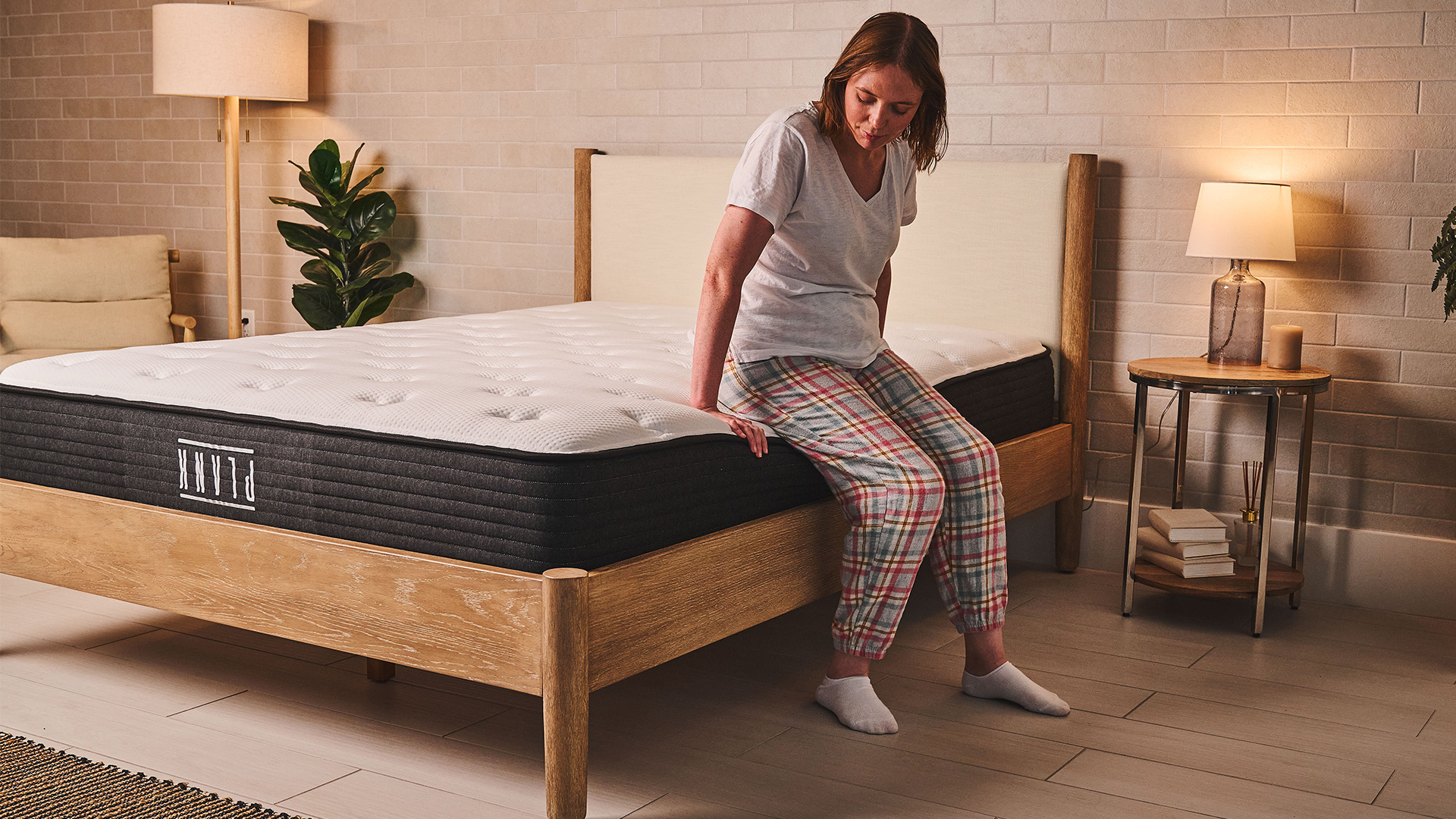 Notre testeur de matelas Ruth Jones est assise sur le côté du matelas Plank Firm sur un cadre de lit dans la chambre. Elle est assise confortablement sur le bord, ce qui indique un bon maintien du bord